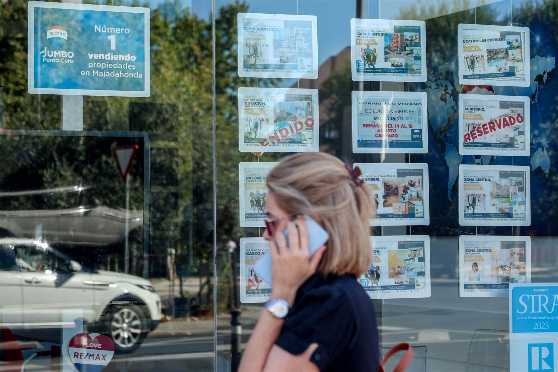 Una mujer camina frente a un escaparate de anuncios de viviendas