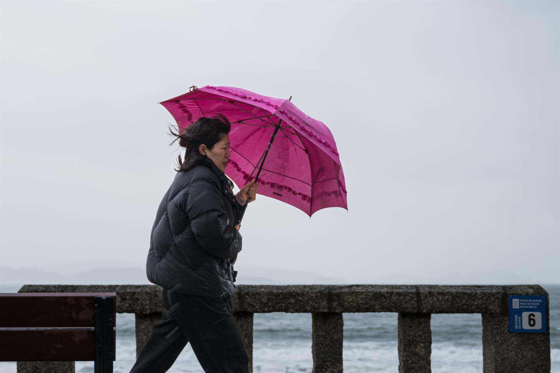 Una mujer se refugia de la lluvia con paraguas en el litoral gallego.
