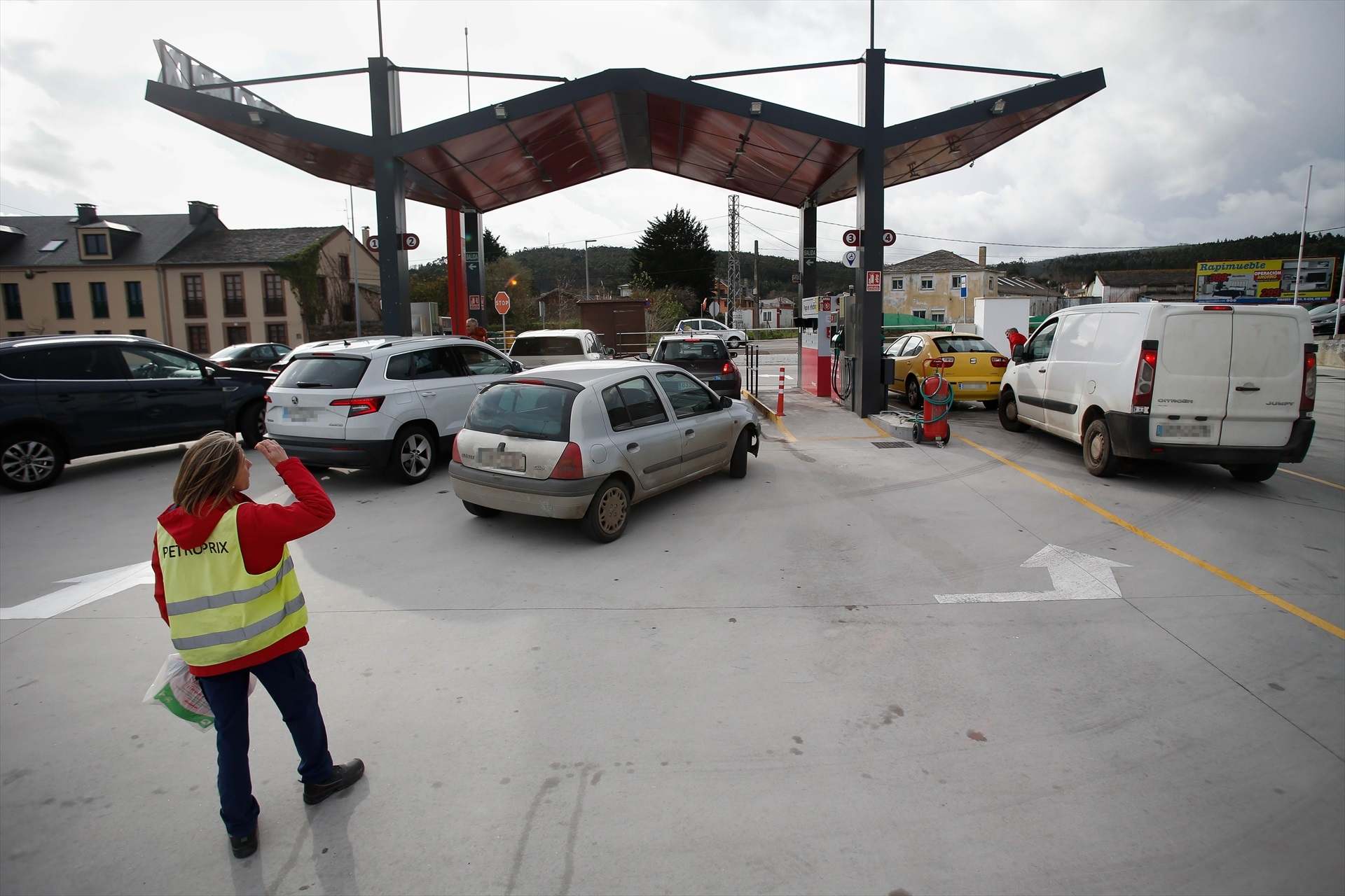 Una trabajadora de PetroPrix junto a coches a punto de repostar. Europa Press