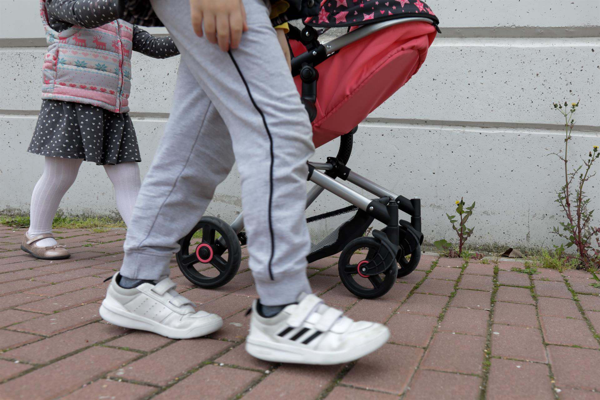 Una niña pasea por la calle empujando un carrito con un bebé de juguete junto a su padre y su hermano.