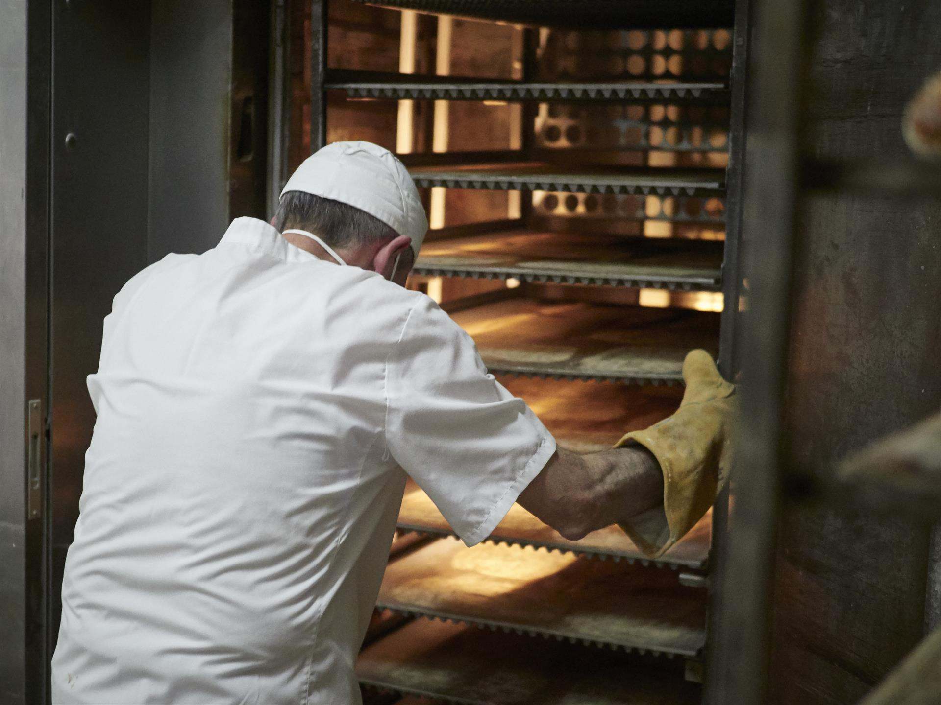 Un panadero maneja bandejas para cocer el pan en el obrador.