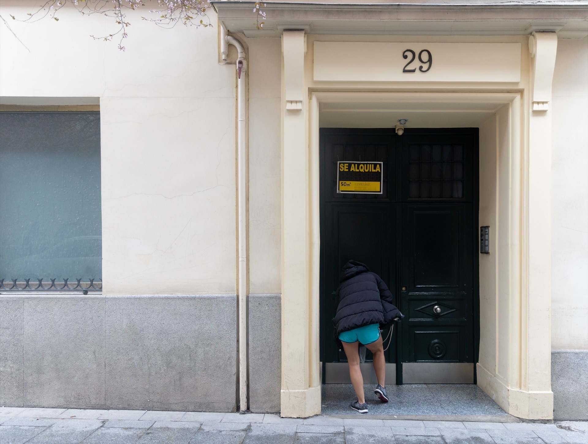 Una mujer entra en un portal con un cartel de "se alquila".