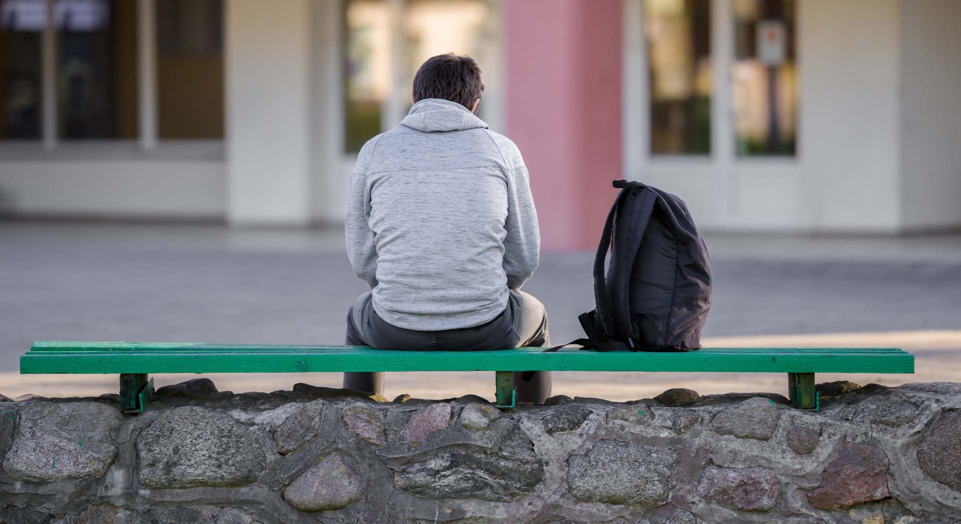 Un hombre solo sentado en un banco junto a una mochila