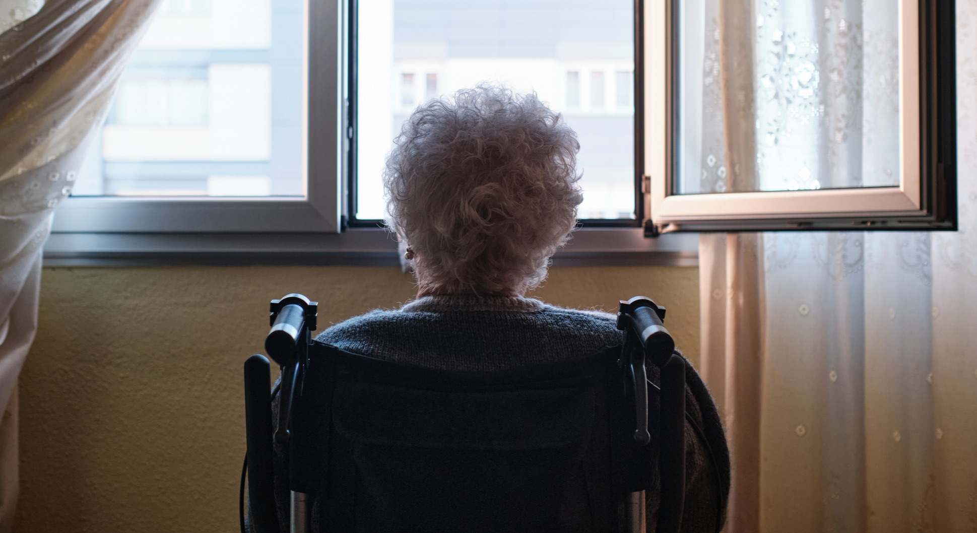 Mujer mayor en silla de ruedas mirando por la ventana