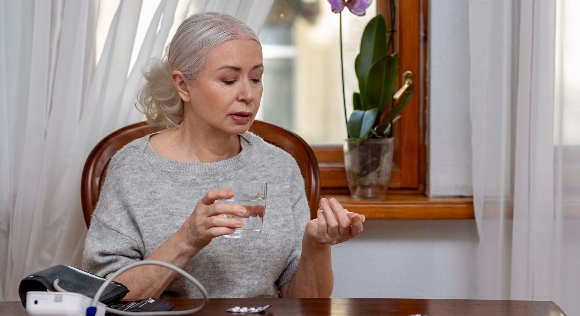 Mujer tomándose la pastilla de la tensión junto con un tensiómetro y un vaso de agua