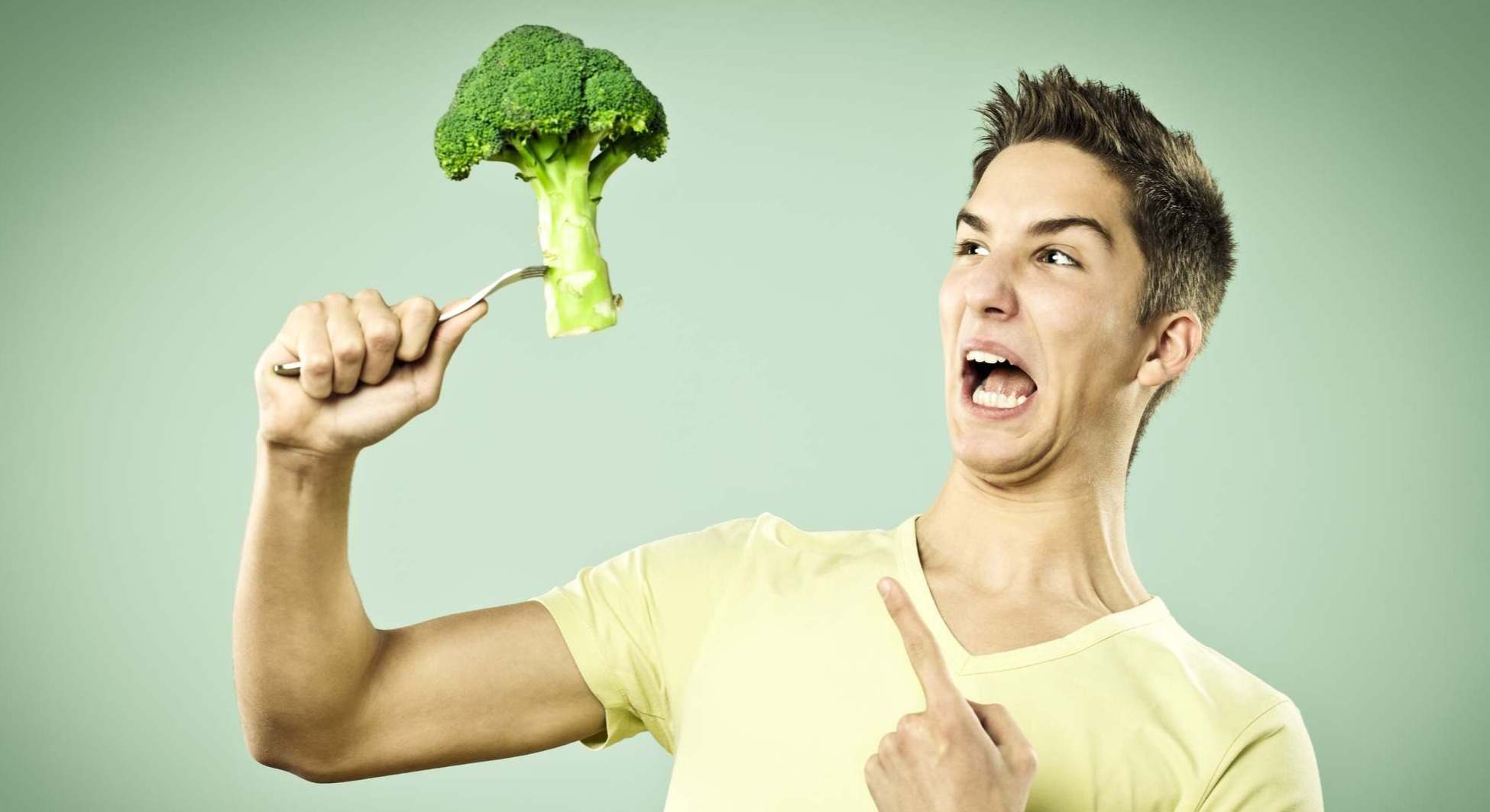 Joven con brocoli en un tenedor con cara de asco