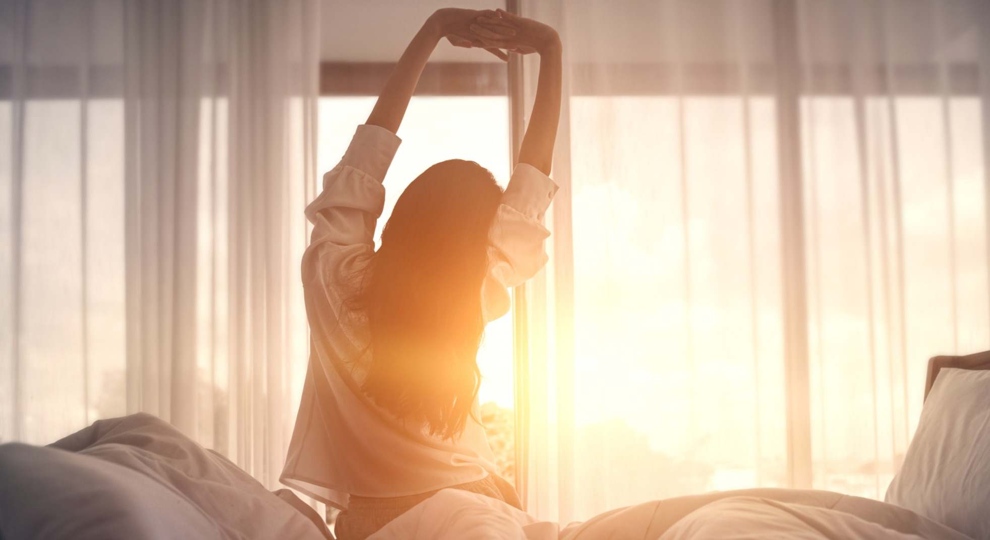 Mujer levantándose temprano por la mañana frente a una ventana