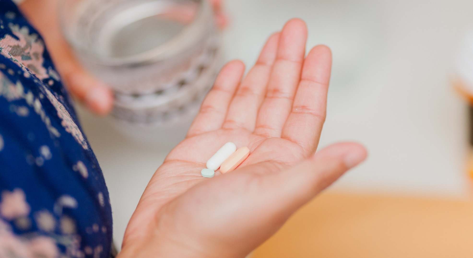 Mano de mujer con tres pastillas y con un vaso de agua en la mano