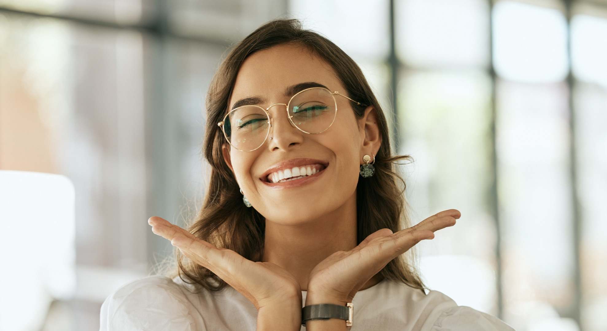 Mujer con gafas sonriendo con las manos debajo de la barbilla