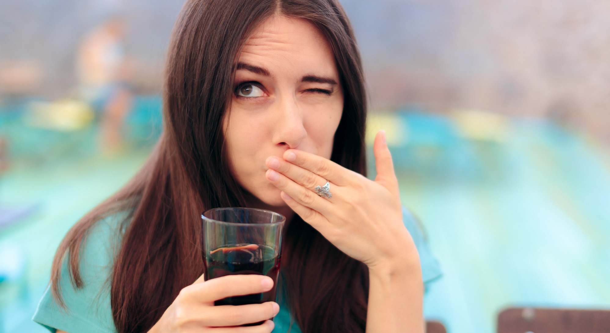 Mujer con un vaso de refresco se tapa la cara al eructar