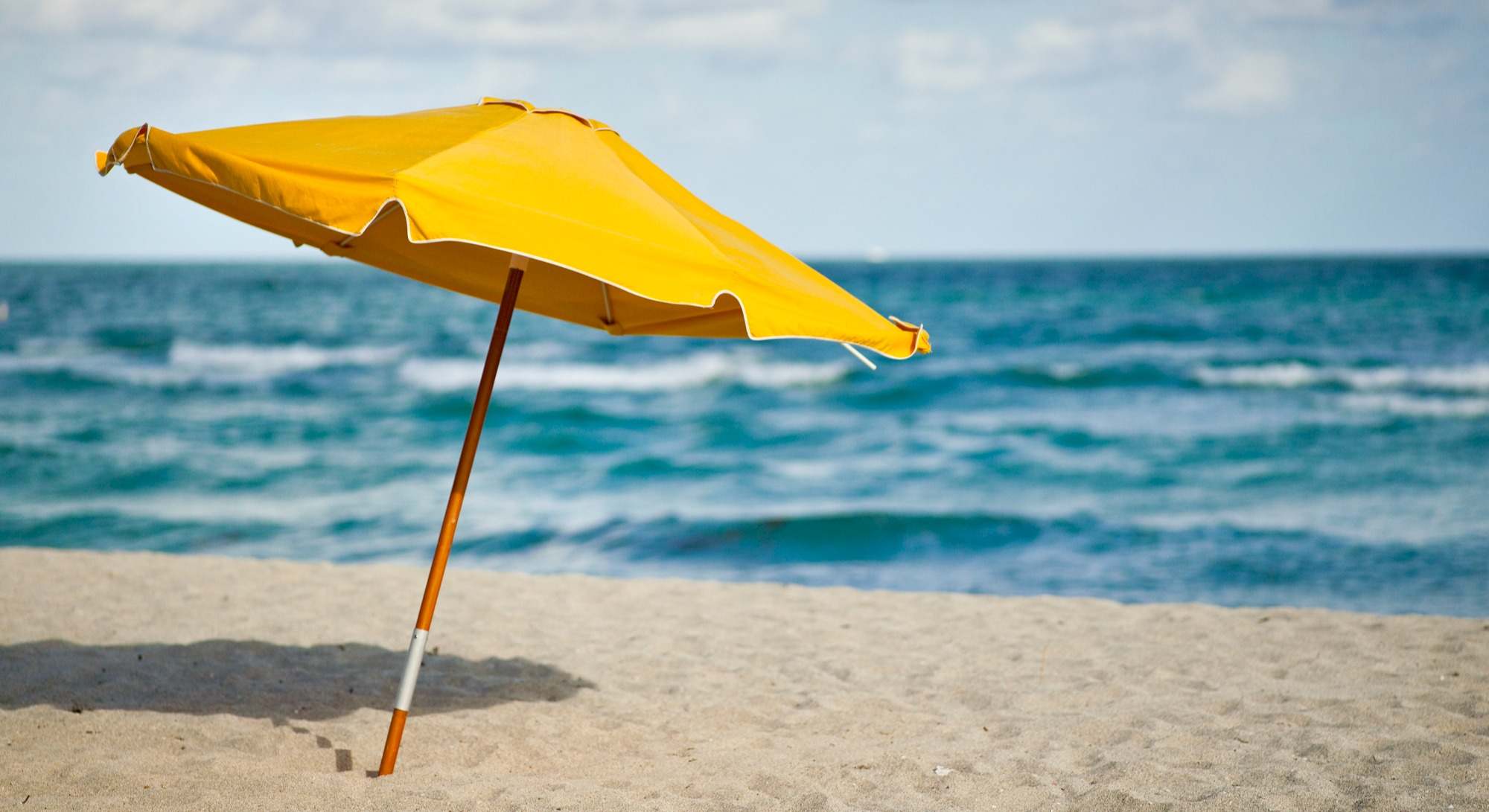 Sombrilla amarilla en primera línea de playa de arena