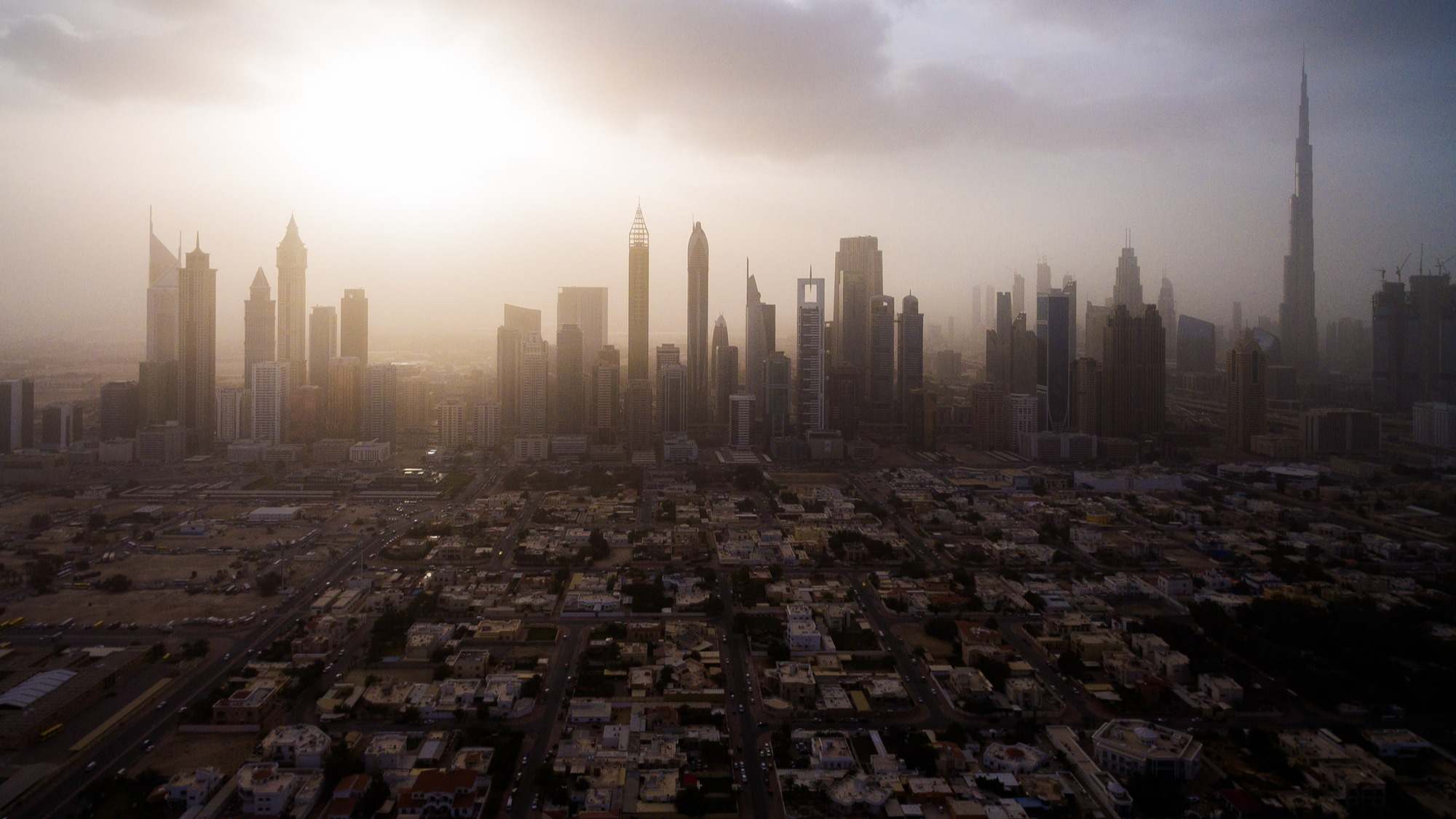 Vista aérea del paisaje urbano, con grandes rascacielos y el sol atravesando las nubes de Dubai