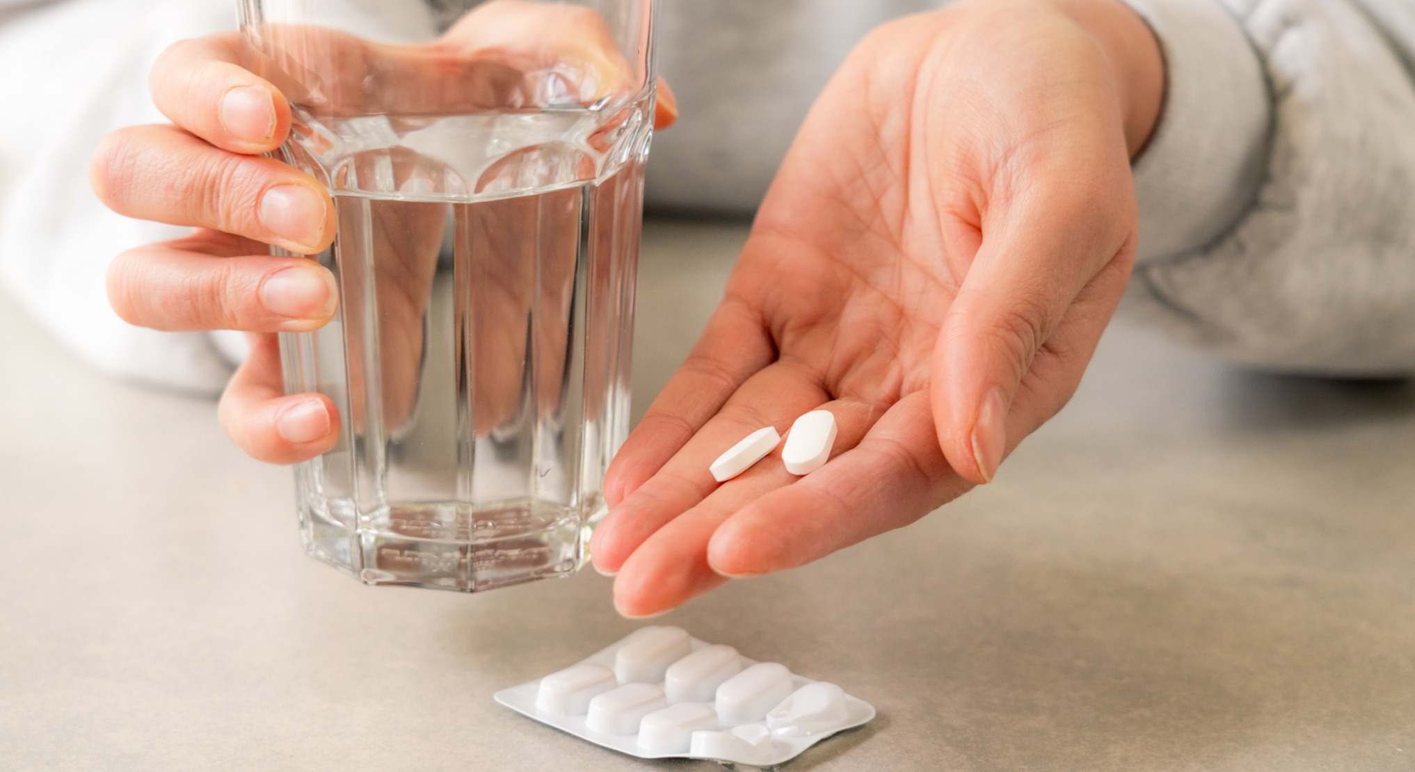 Manos con un vaso de agua y pastillas de ibuprofeno