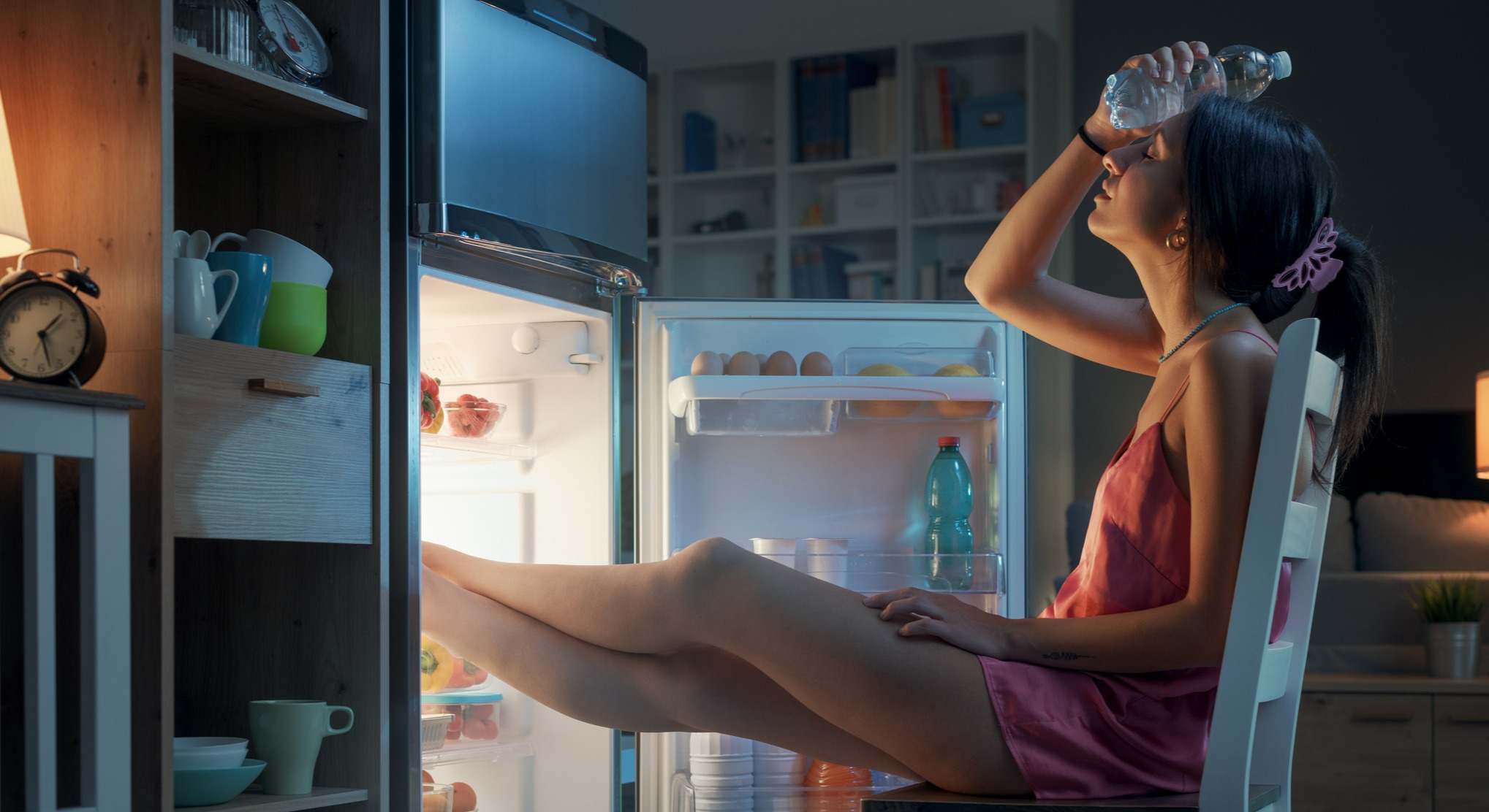 Mujer sentada frente a la nevera abierta con mucho calor