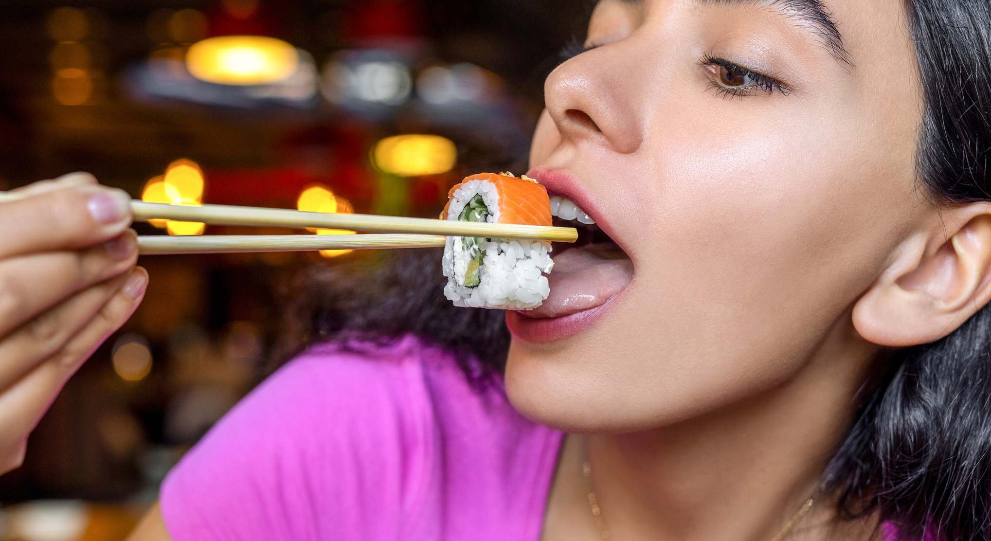 Mujer comiendo una pieza de sushi con palillos