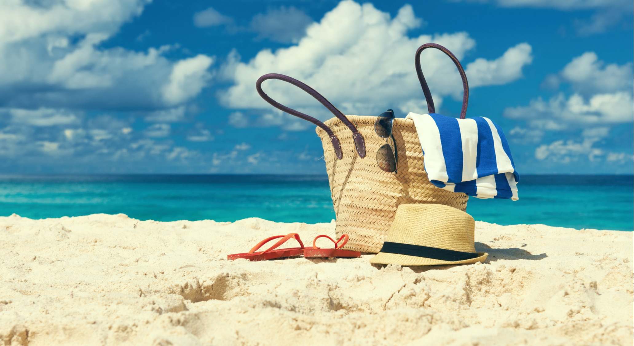 Cesta con toallas, gafas, sombrero, chanclas y gafas de sol sobre la arena de una playa