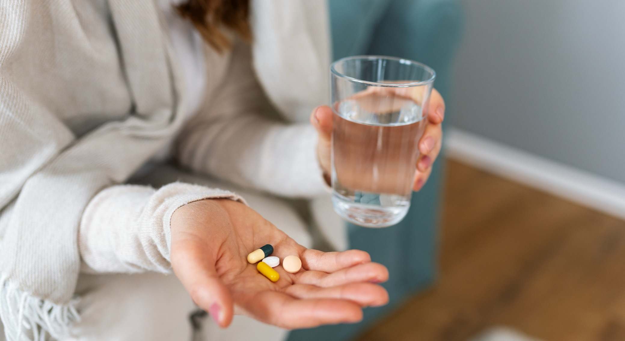 Una mujer con pastillas y un vaso de agua en la mano