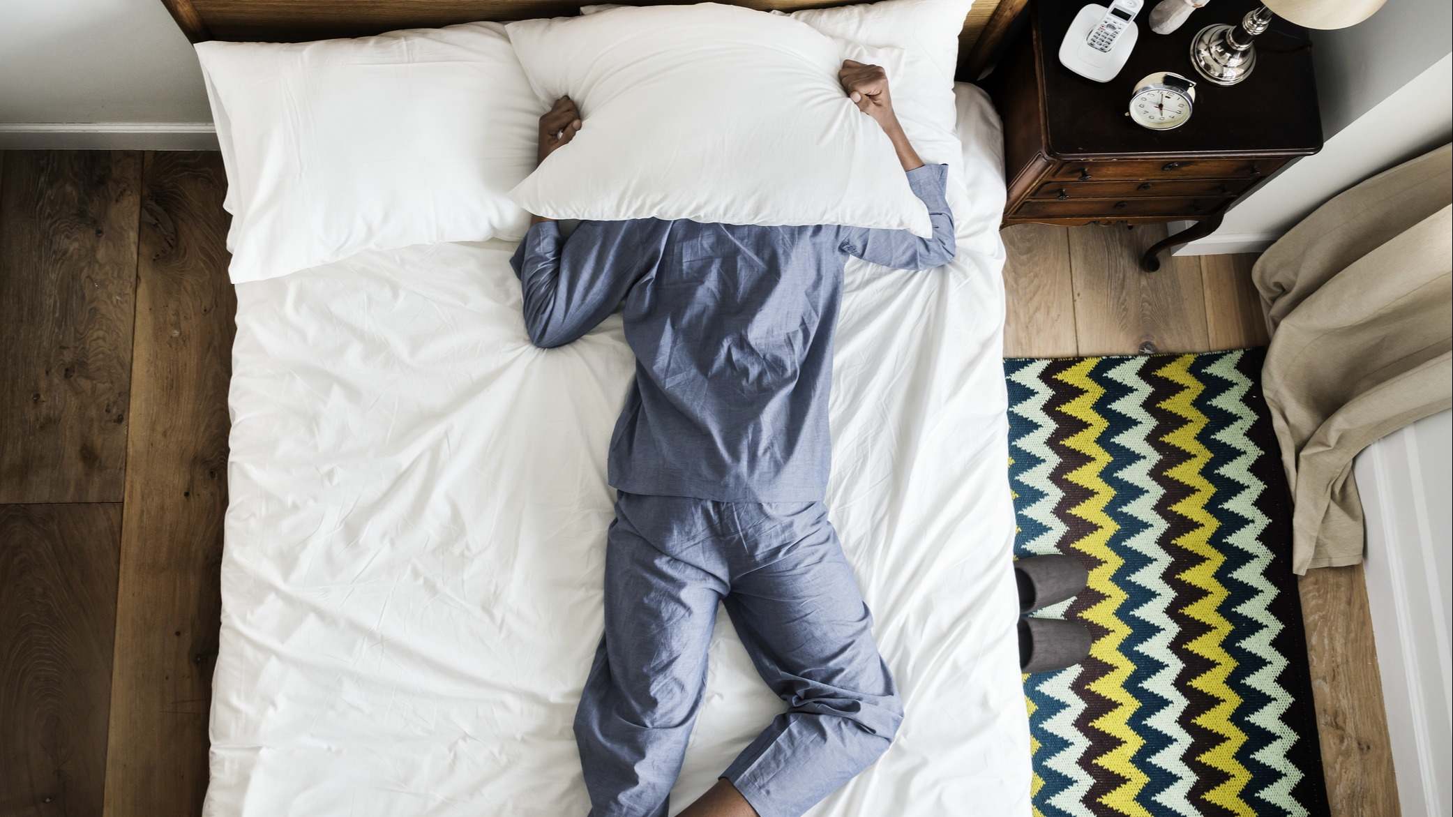 Hombre tirado en la cama con insomnio con una almohada tapando su cara
