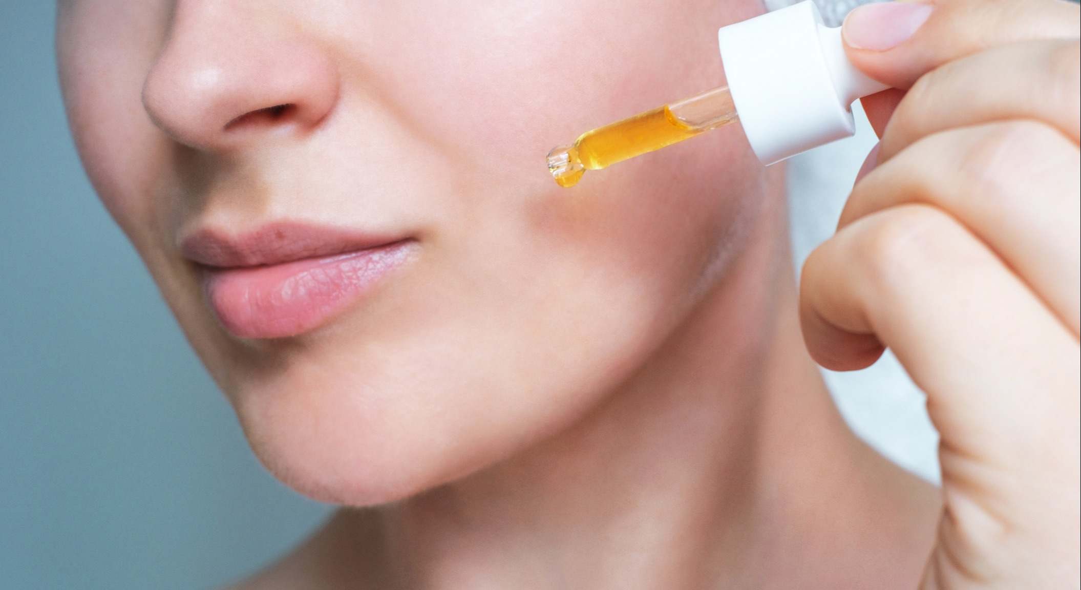 Rostro femenino y gotero con primer plano de retinol sobre fondo gris.