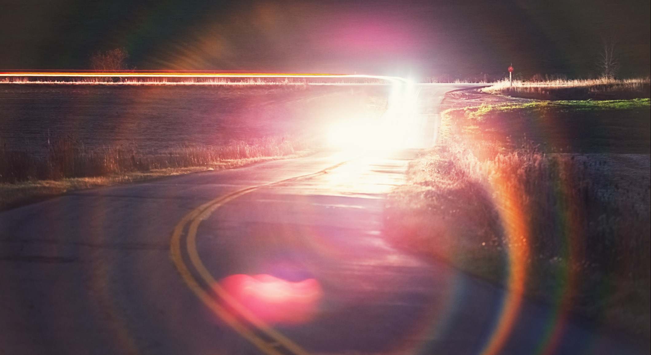 Camino rural con un coche con las luces largas
