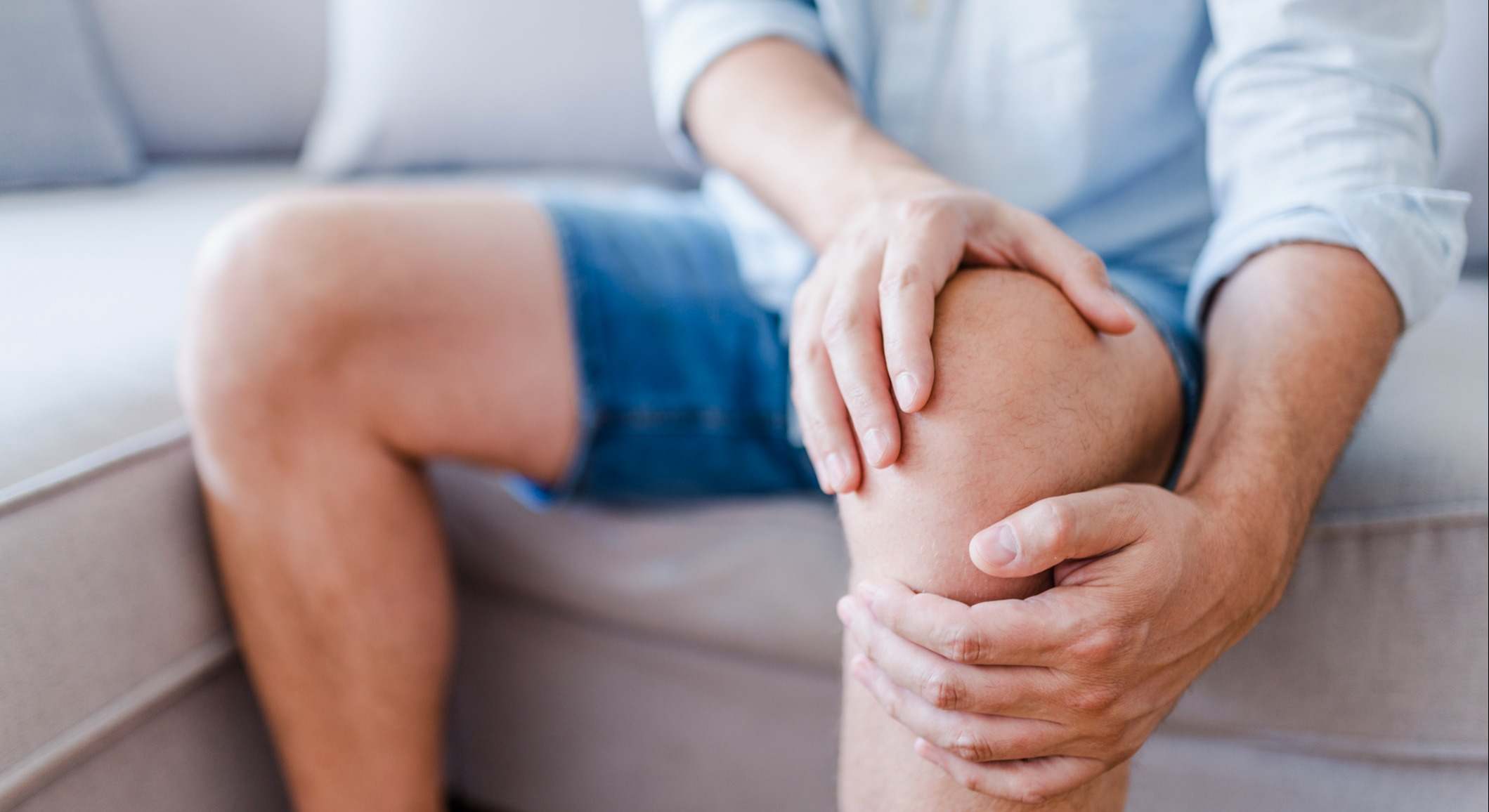 Hombre que sufre dolor de rodilla sentado sofá