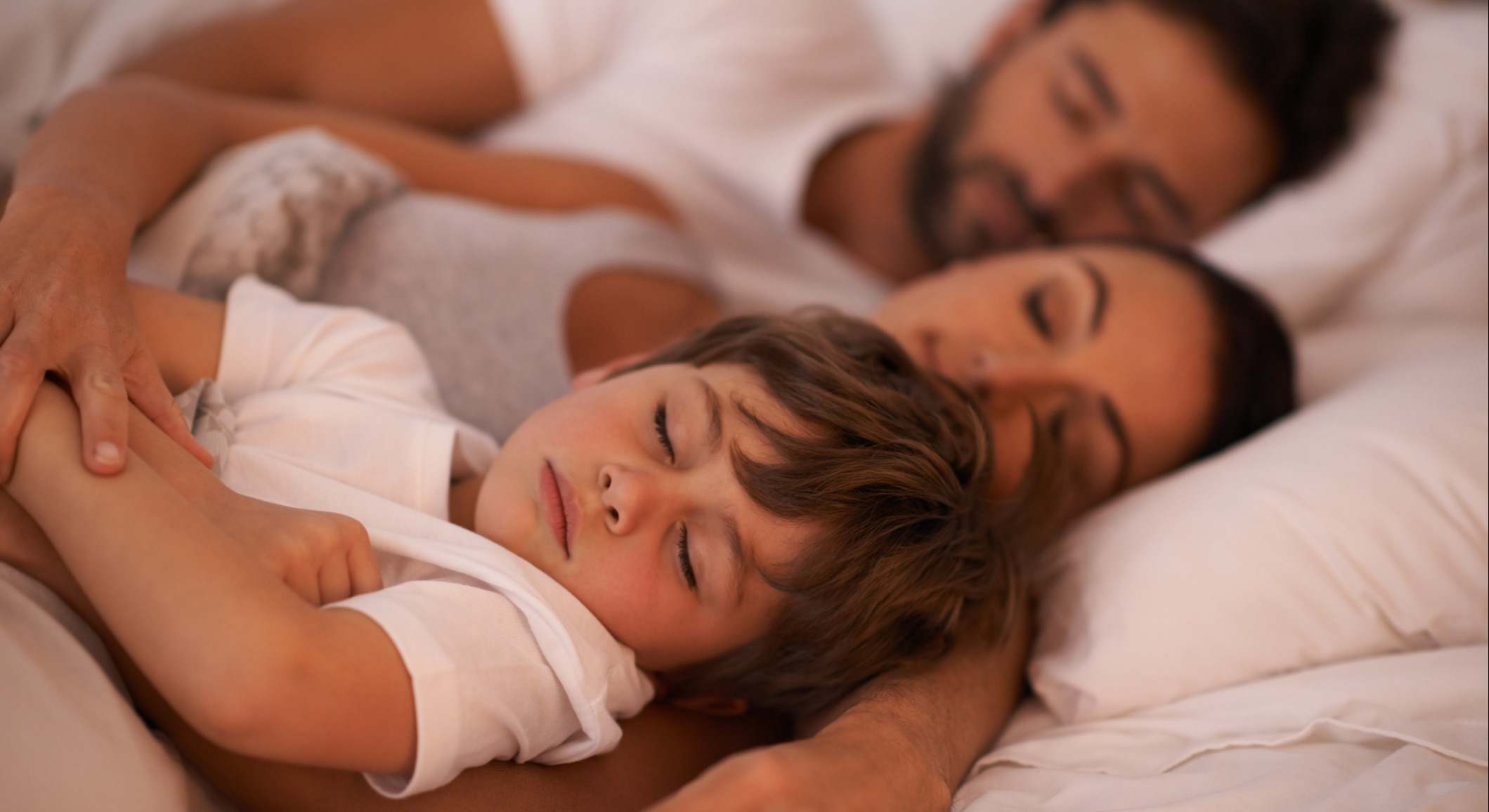 Niño dormido en la cama junto a sus padres