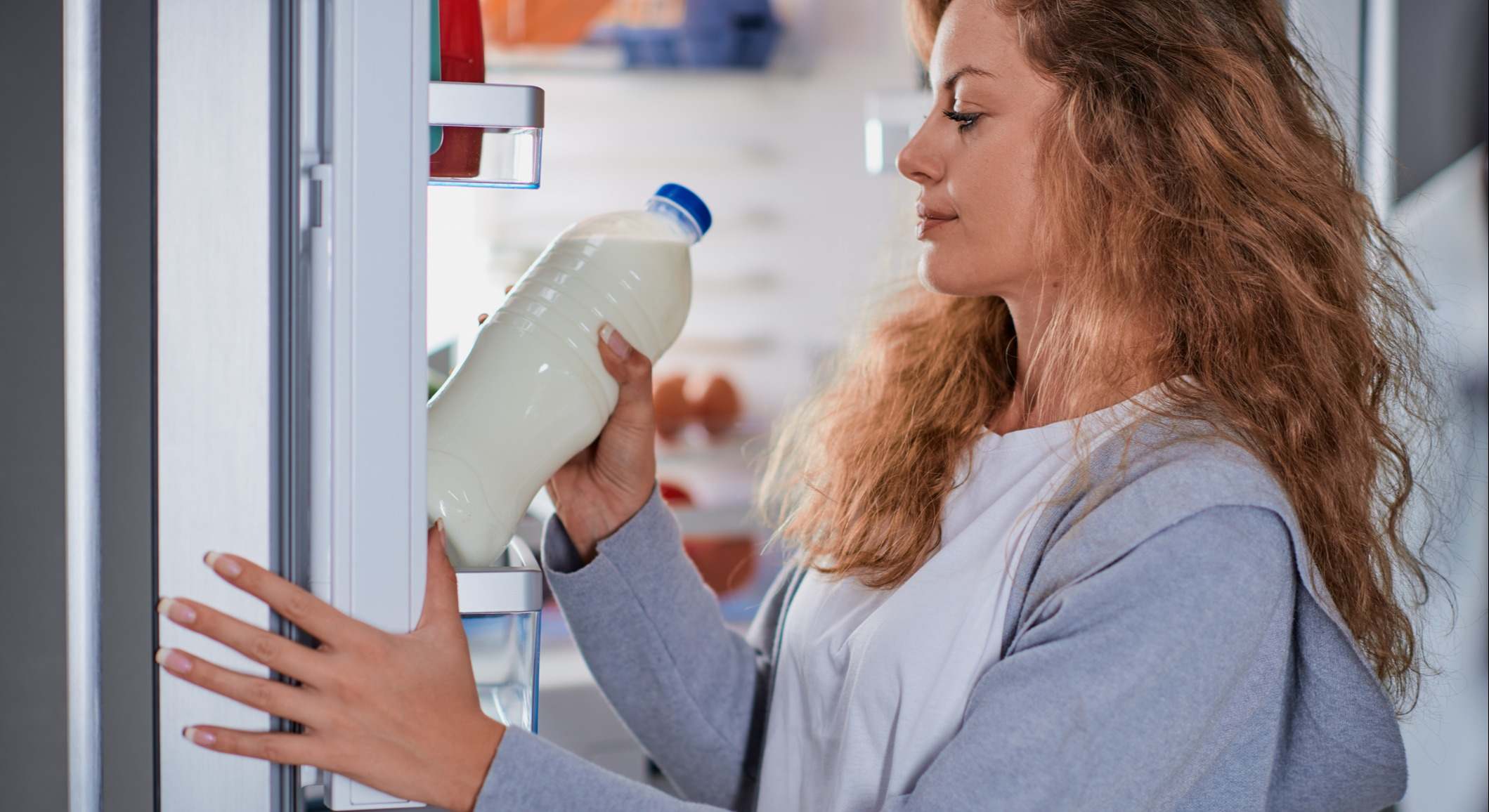 Mujer de pie delante de la nevera guardando una botella de leche
