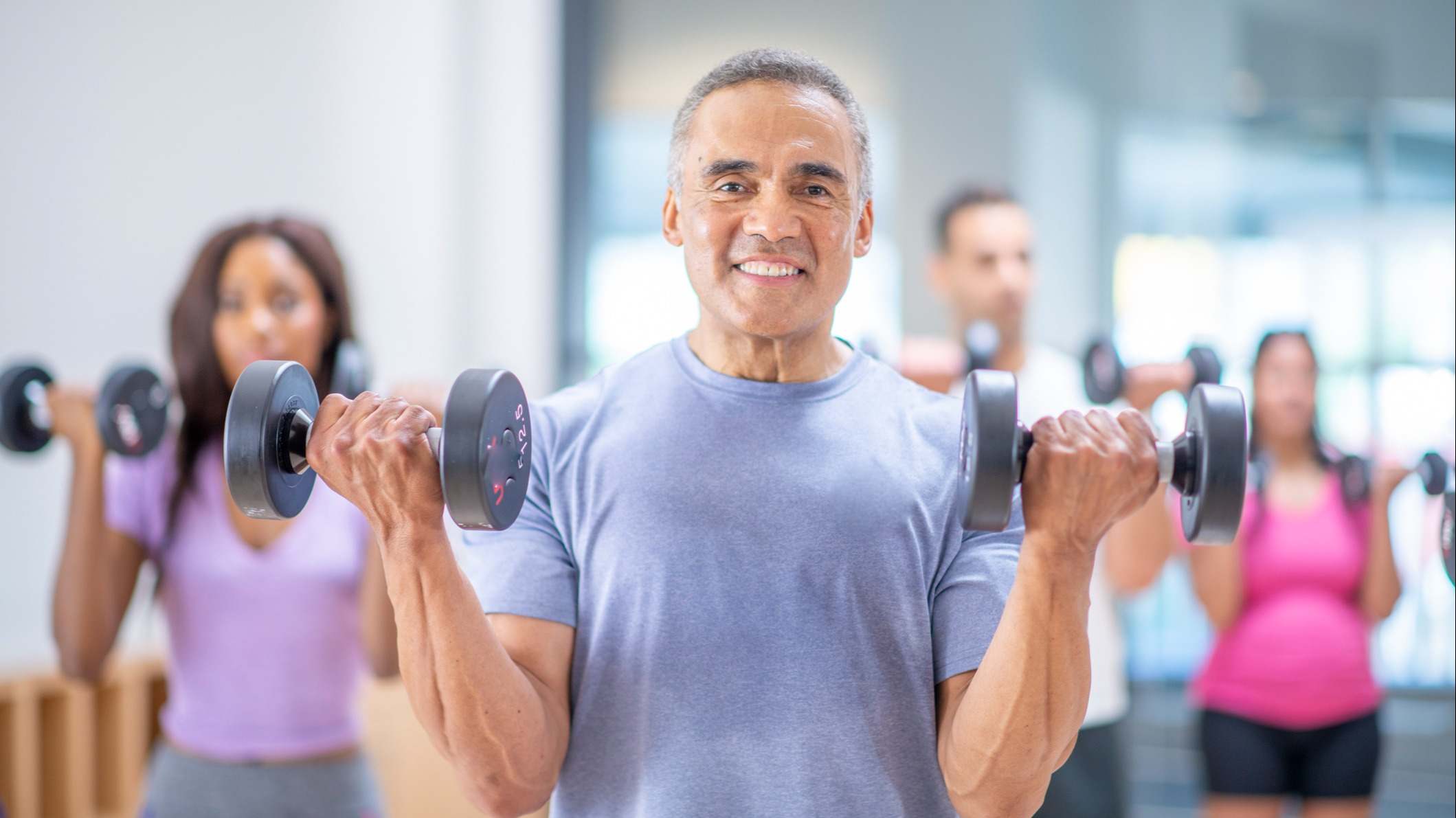 Hombre mayor levantando pesas con cada brazo en un clase de un gimnasio