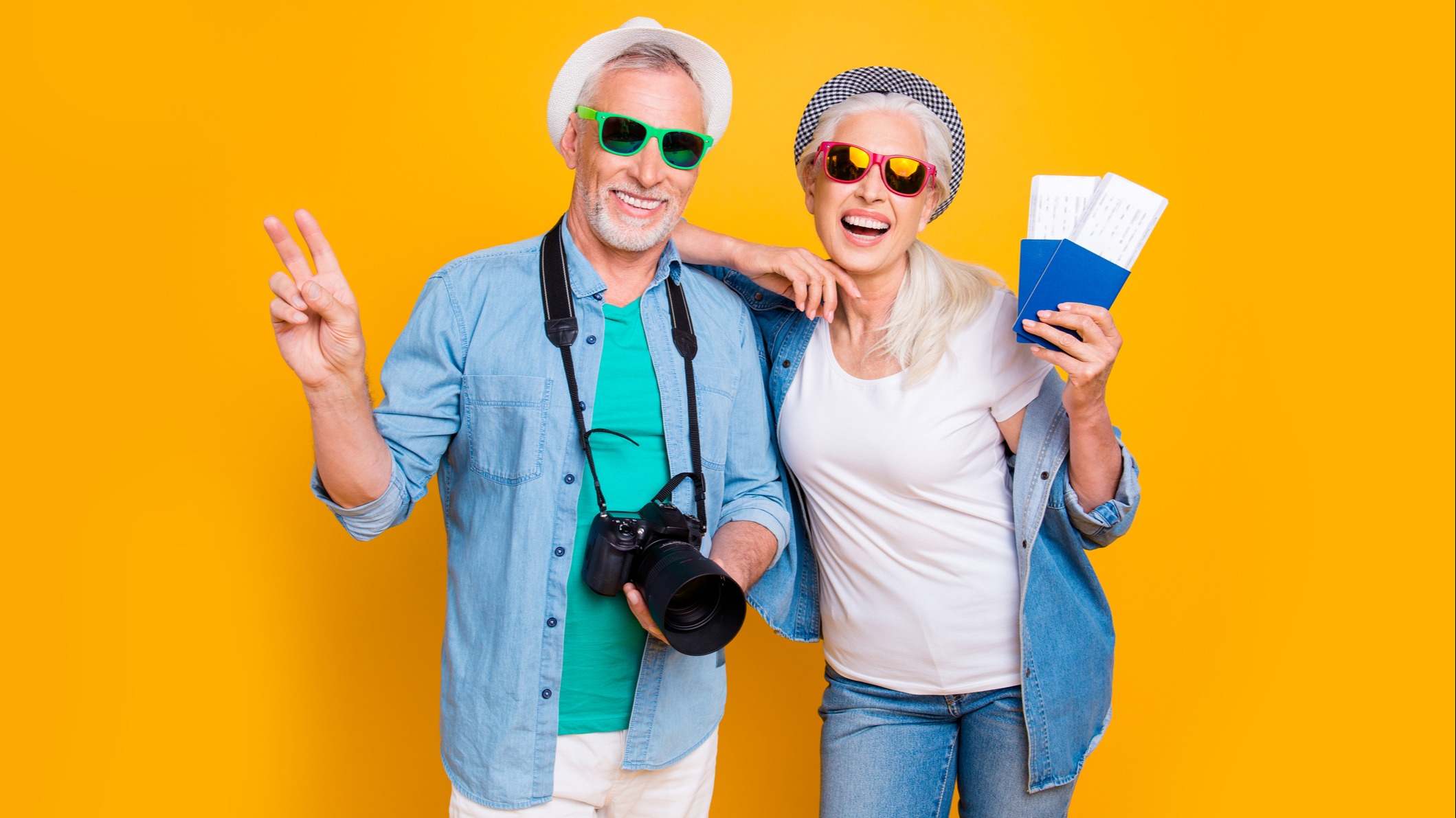 Pareja preparados para un viaje con gorros, gafas de sol, cámara de fotos y billetes de avión