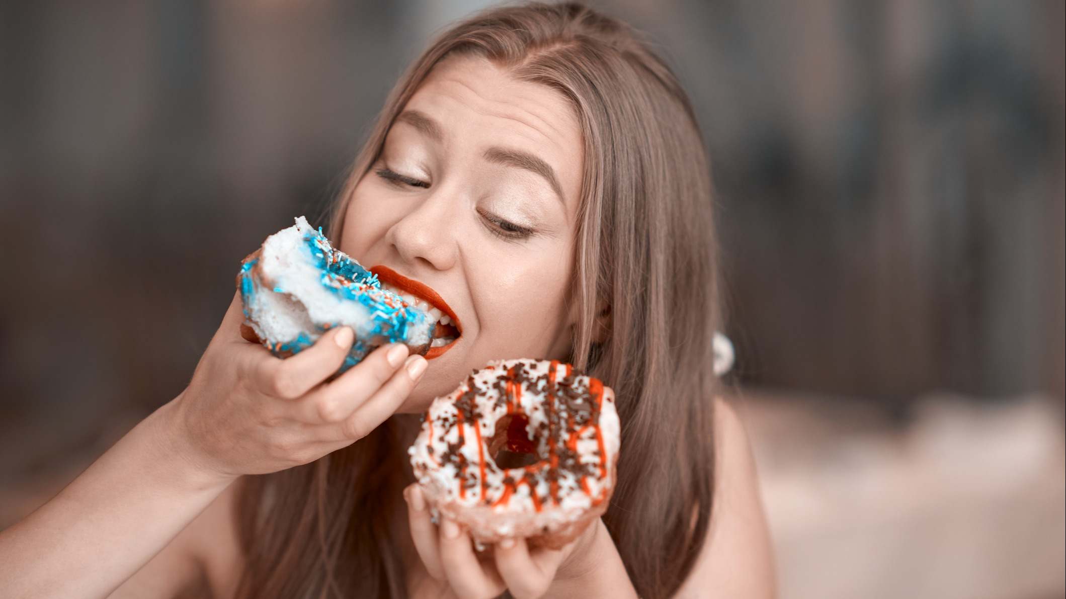 Joven comiéndose un donut mientras sujeta otro con la otra mano