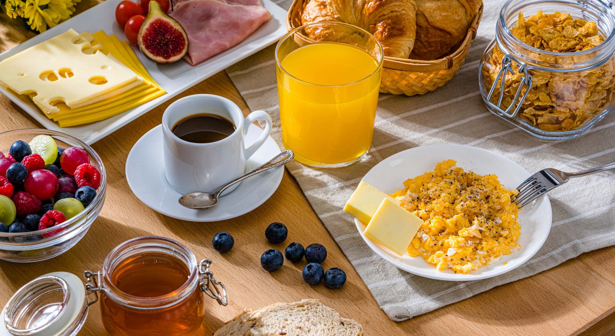 Desayuno saludable a base de huevos revueltos, queso, jamón, café, croissants y zumo de frutas