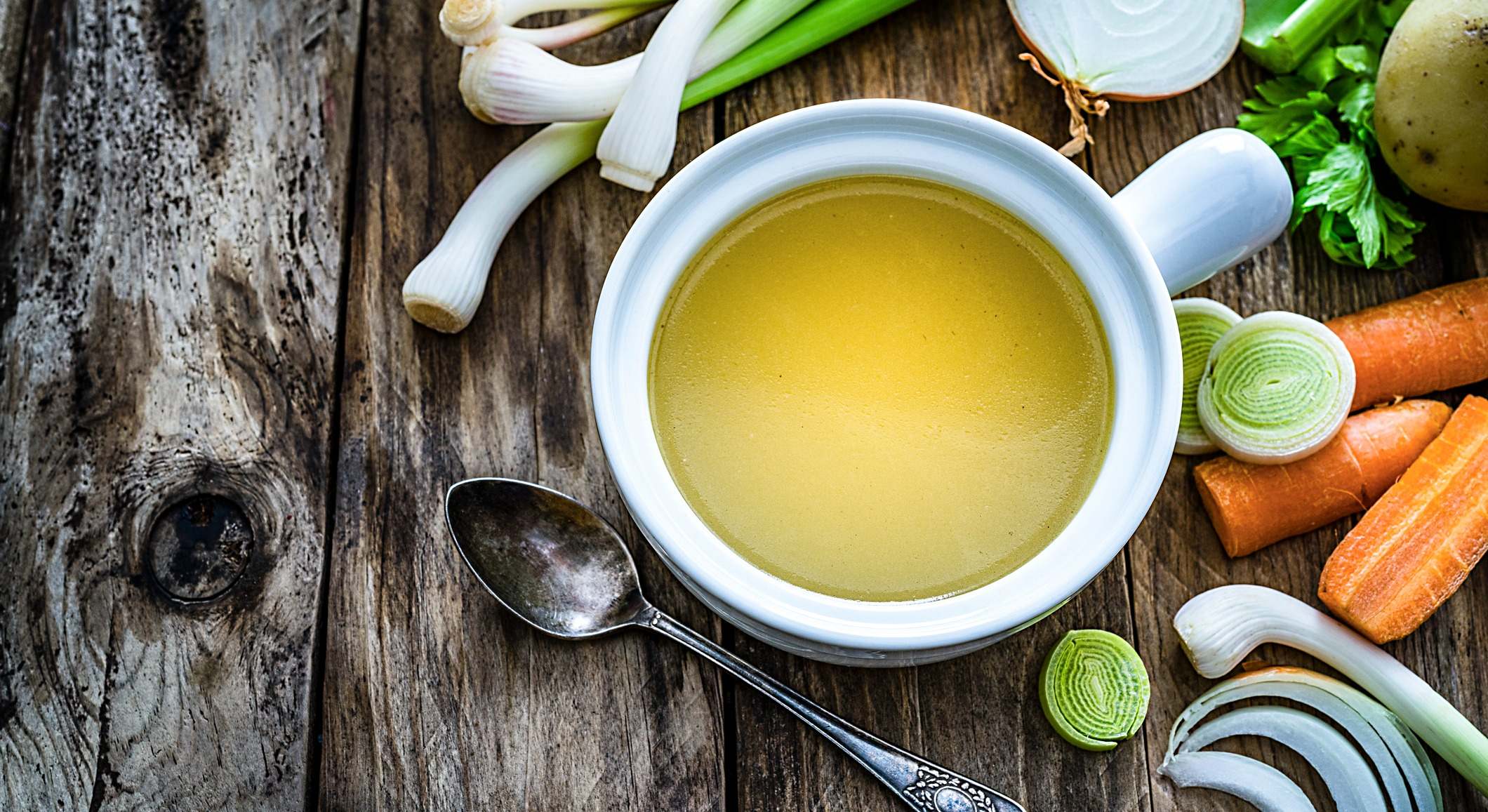 Caldo de verduras con ingredientes en mesa de cocina rústica