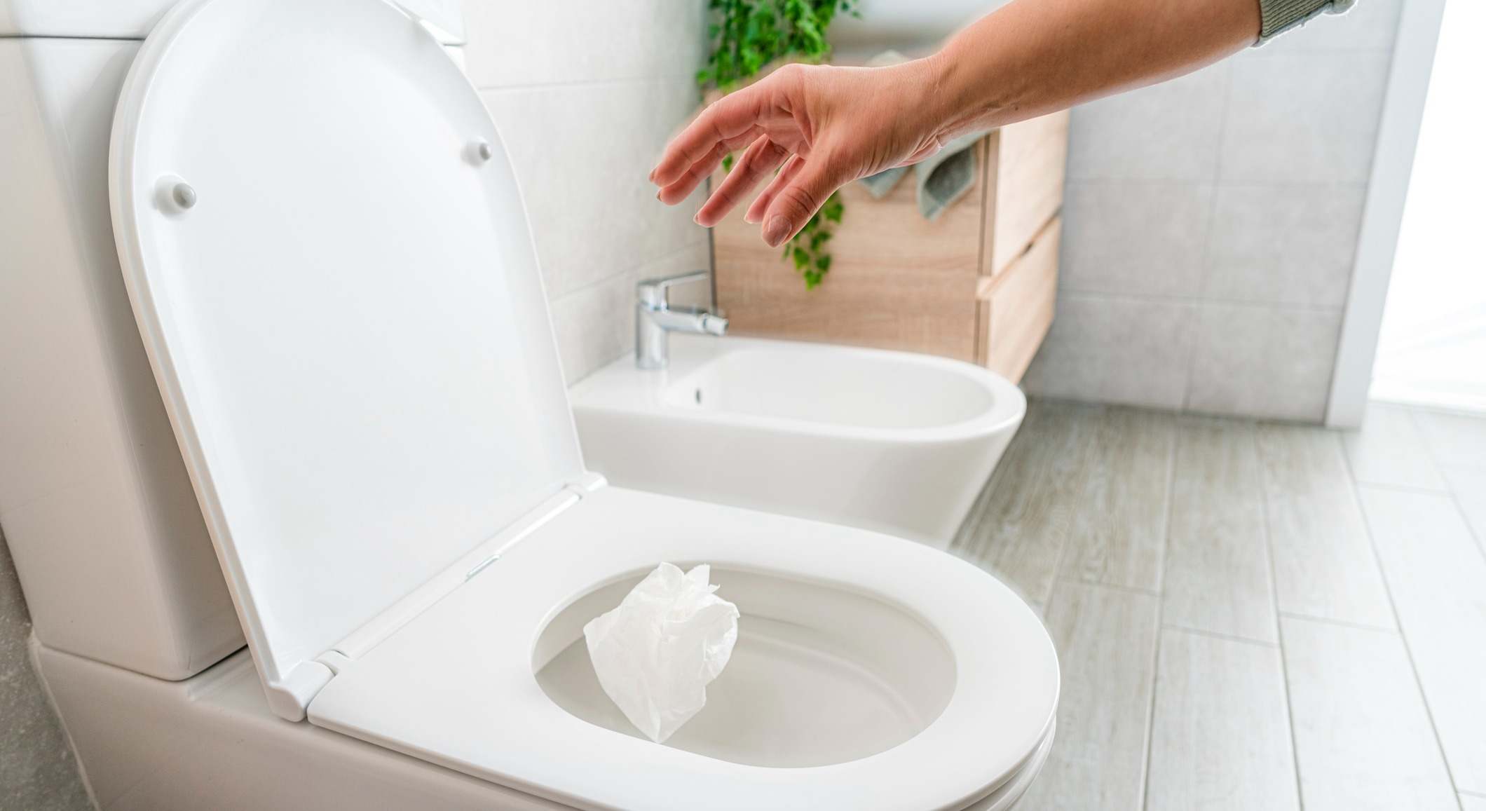Primer plano de la mano de la mujer que deja caer el papel higiénico en la taza del inodoro