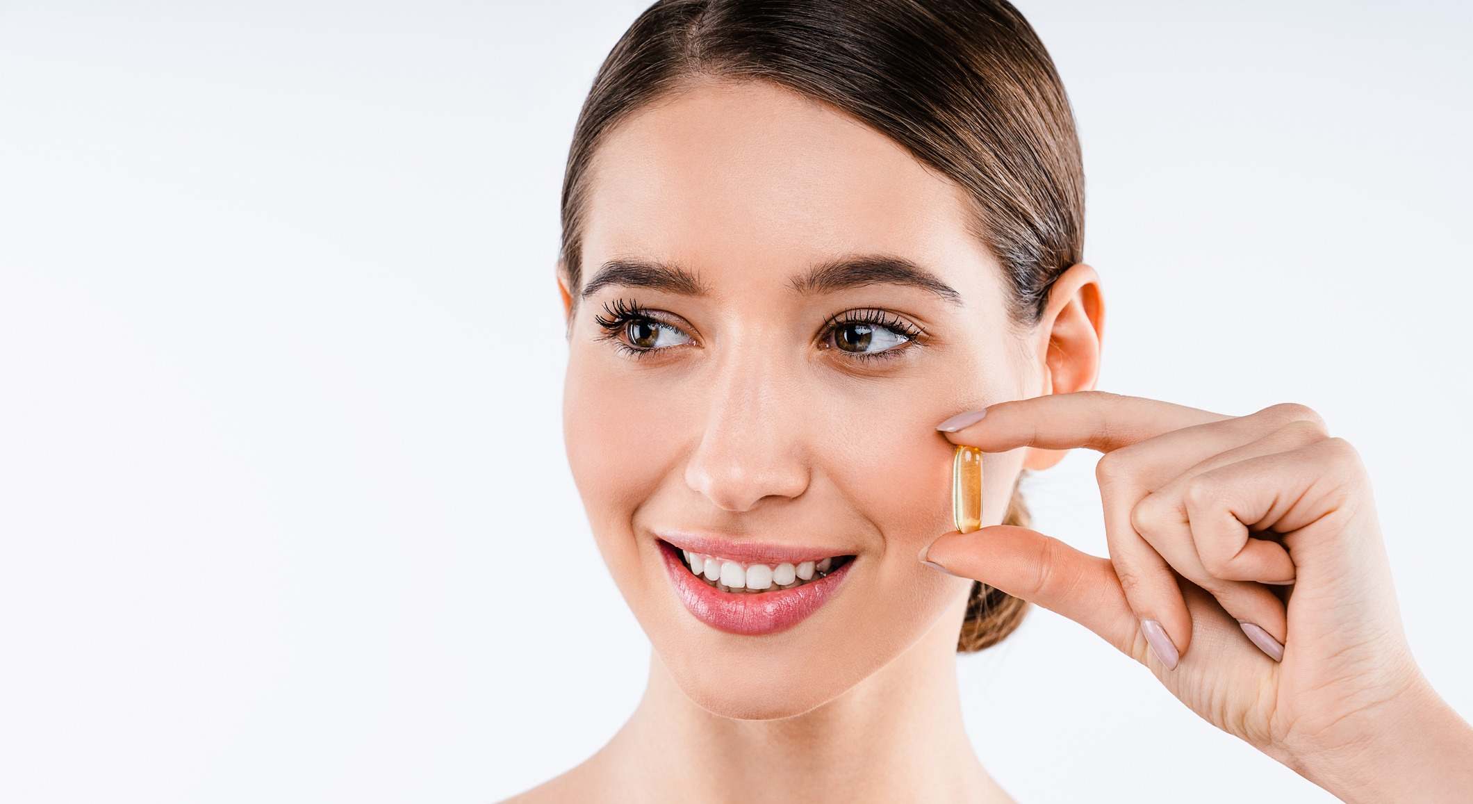 Mujer sosteniendo una vitamina con los dedos sobre su cara