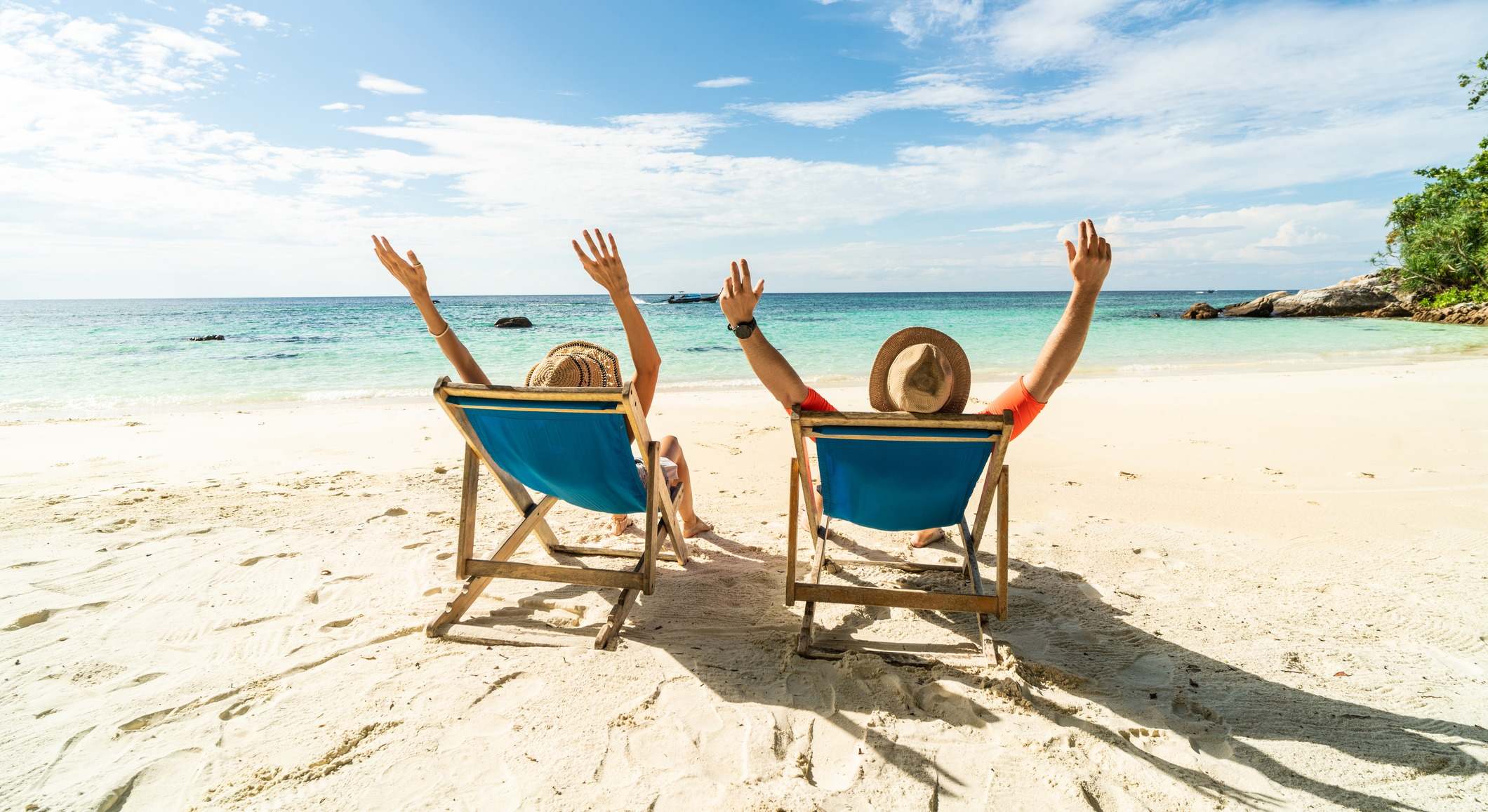 Dos personas felices divirtiéndose en la playa, sentadas en una tumbona azul con las manos levantadas