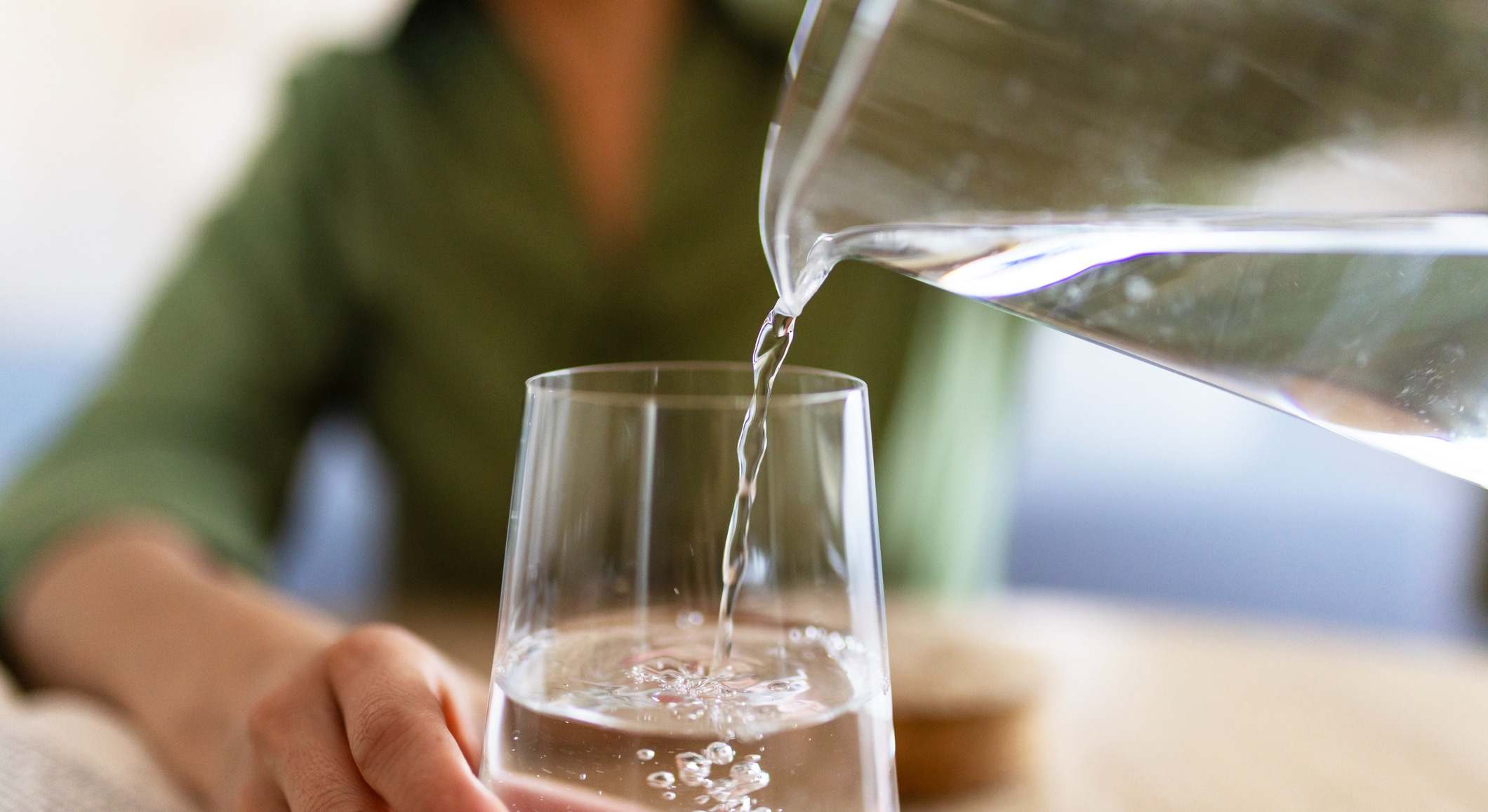 Mujer con camisa verde sirviendo agua de una jarra de cristal