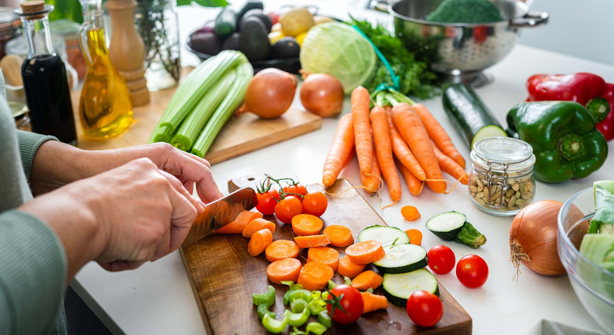 Primer plano de las manos de la mujer cortando zanahorias en la encimera de la cocina