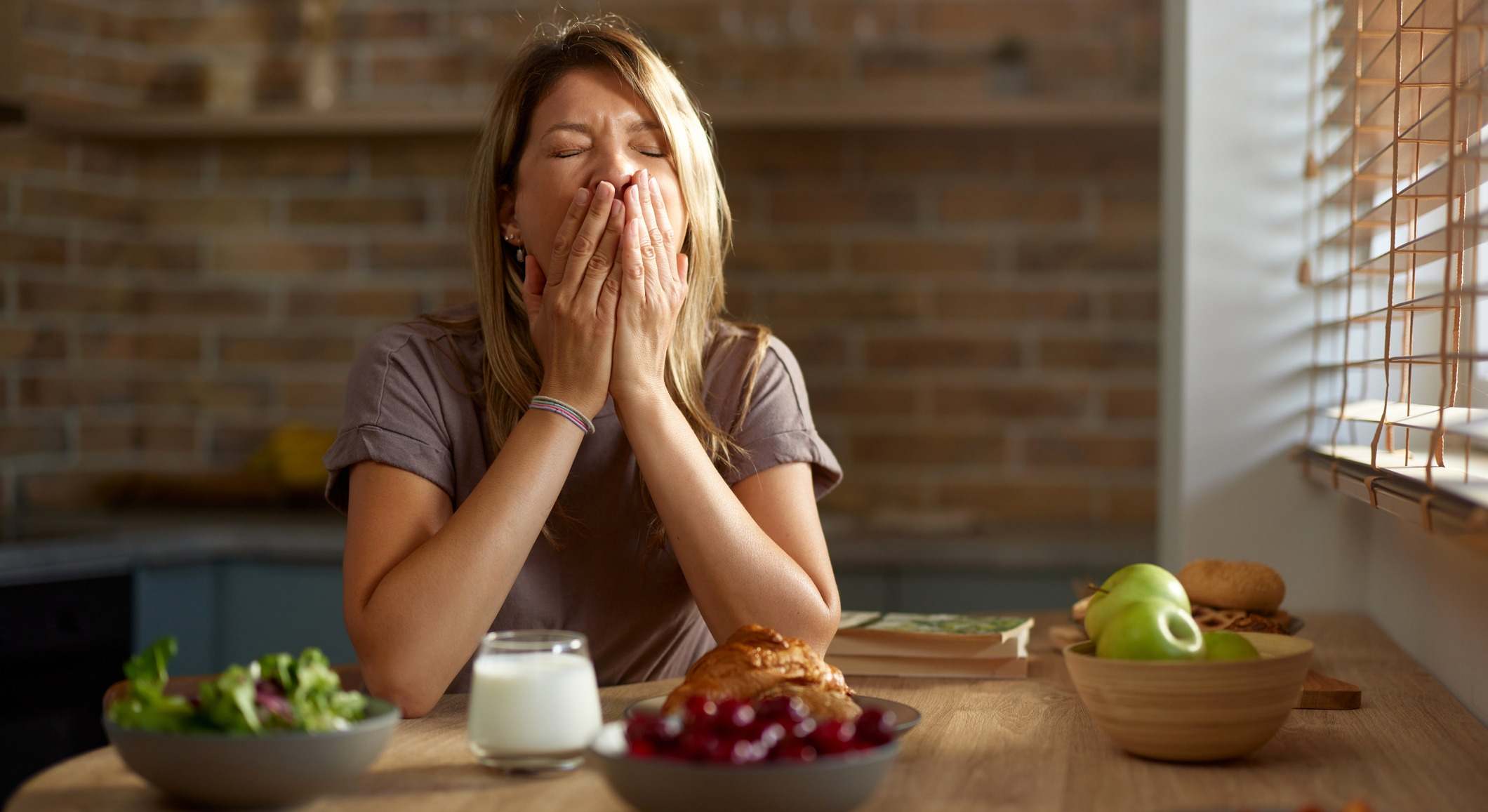 Mujer cansada bostezando durante el desayuno en la mesa del comedor