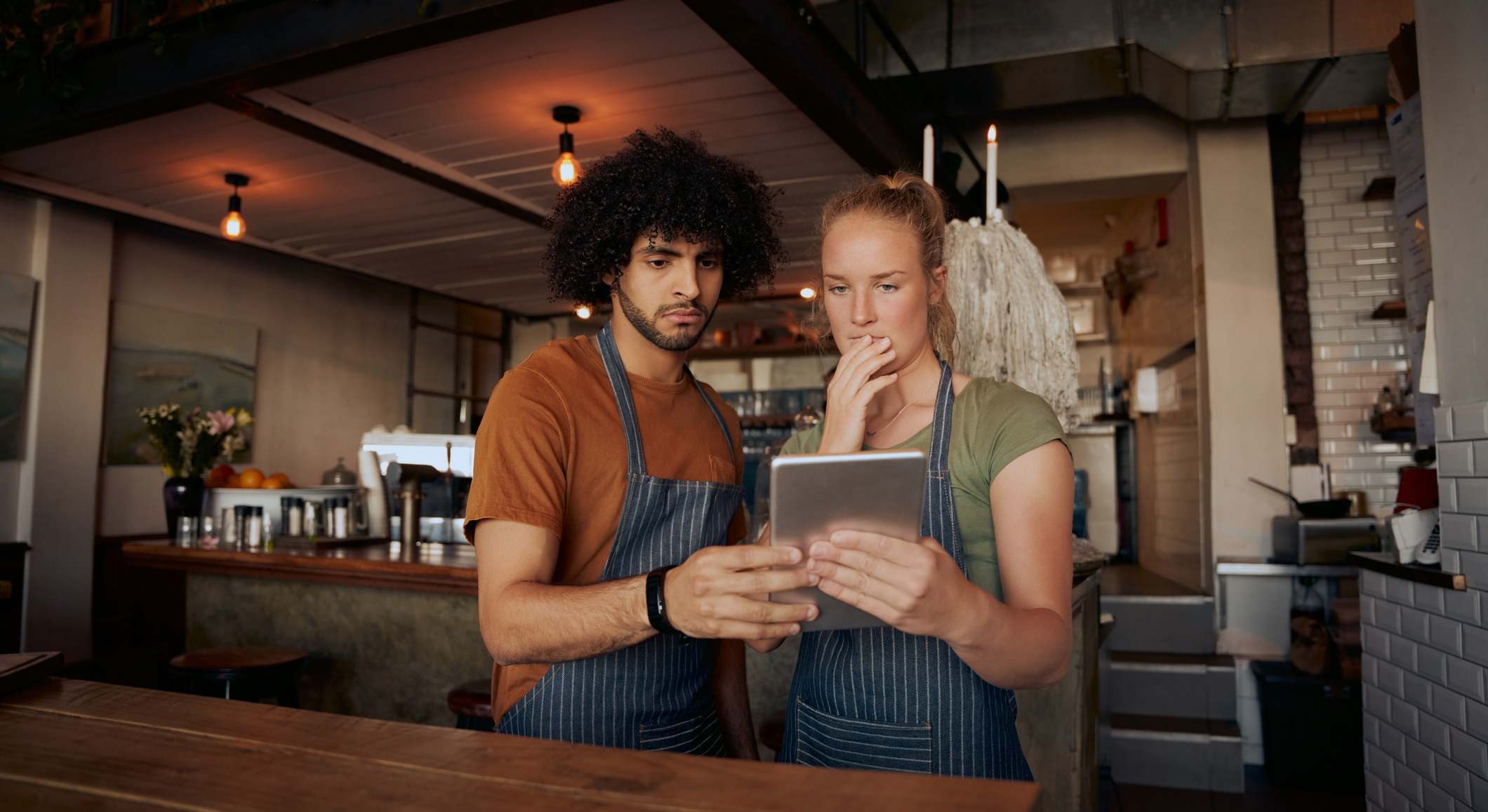 Jóvenes compañeros de trabajo serios que usan tabletas digitales mientras están de pie en un café