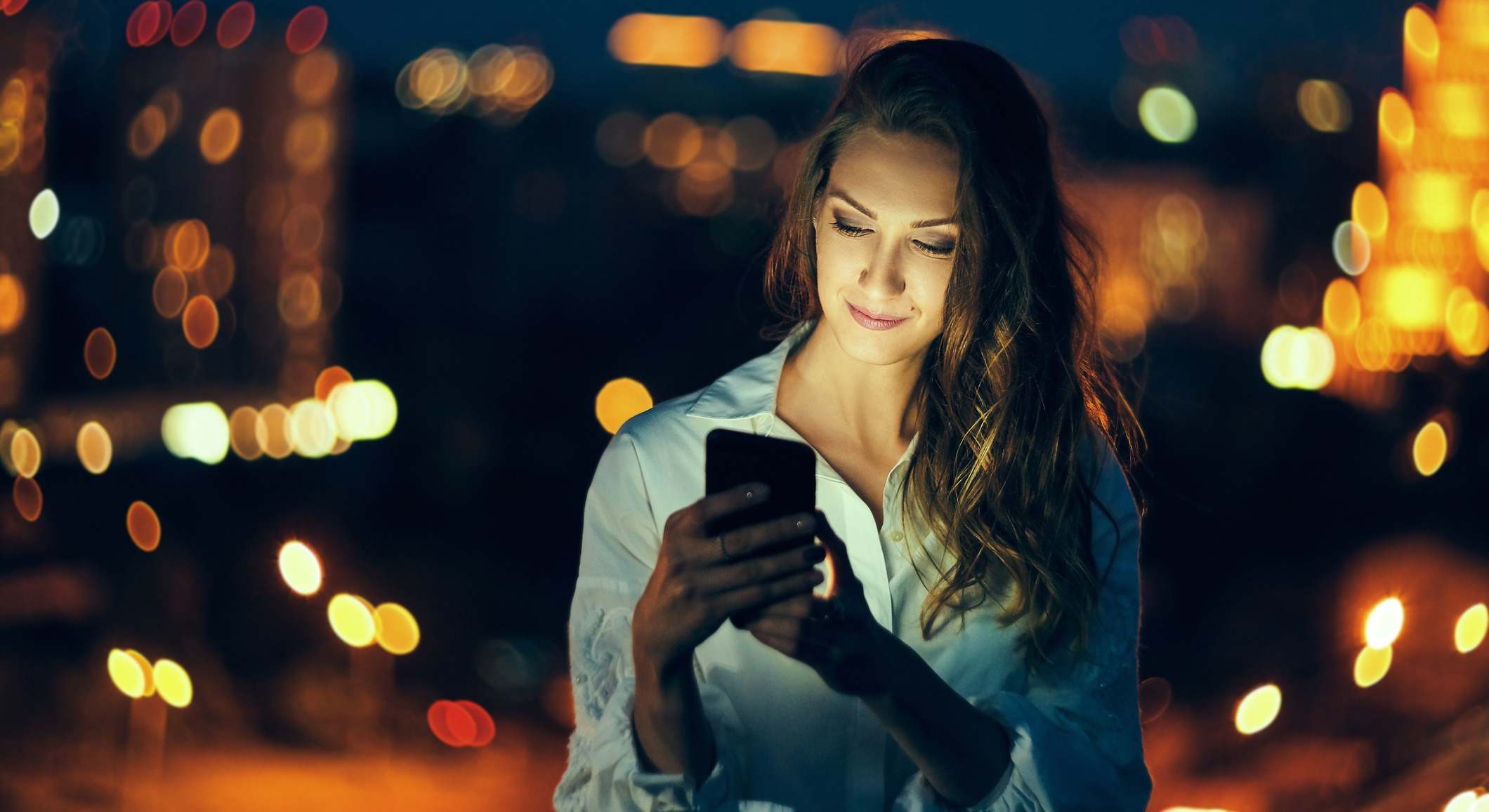 Mujer con la cara iluminada por utilizar el teléfono por la noche