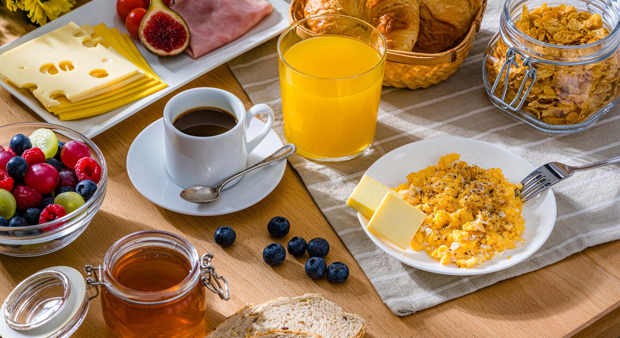 Desayuno saludable a base de huevos revueltos, queso, jamón, café, croissants y zumo de frutas