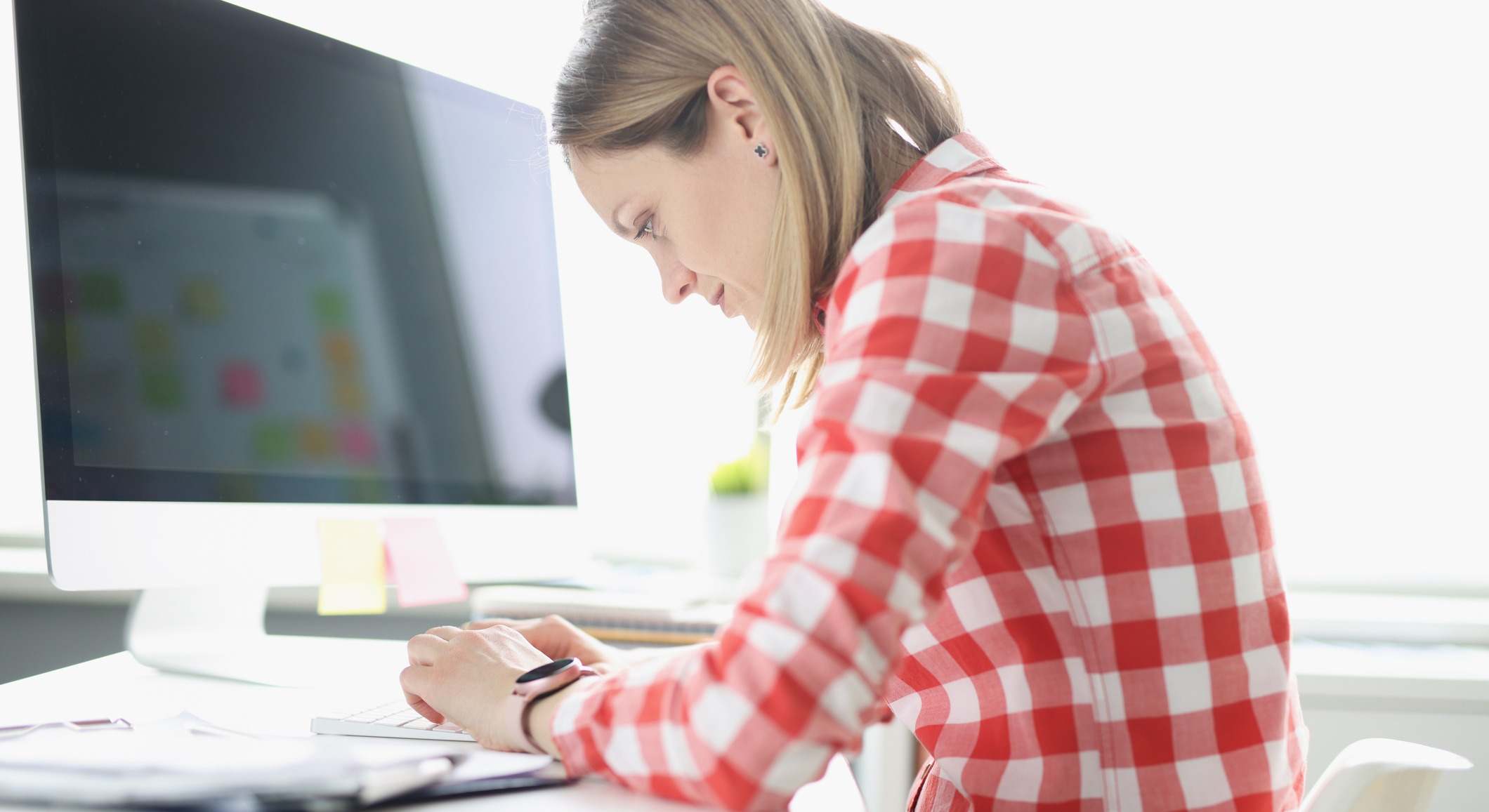 Mujer encorvada escribiendo en el teclado de una ordenador en la mesa