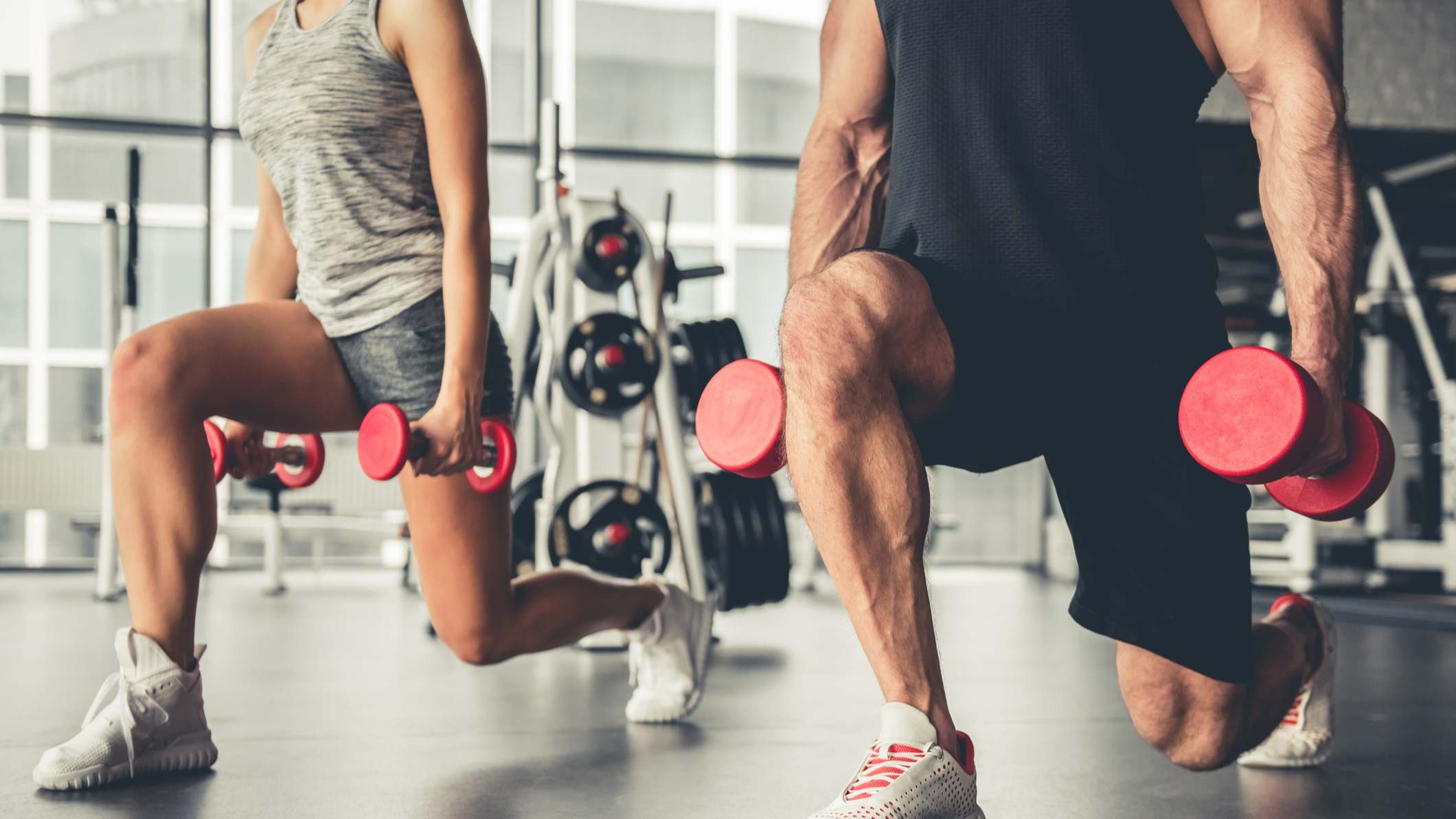 Hombre y mujer realizando un ejercicio físico con pesas en ambas manos en un gimnasio