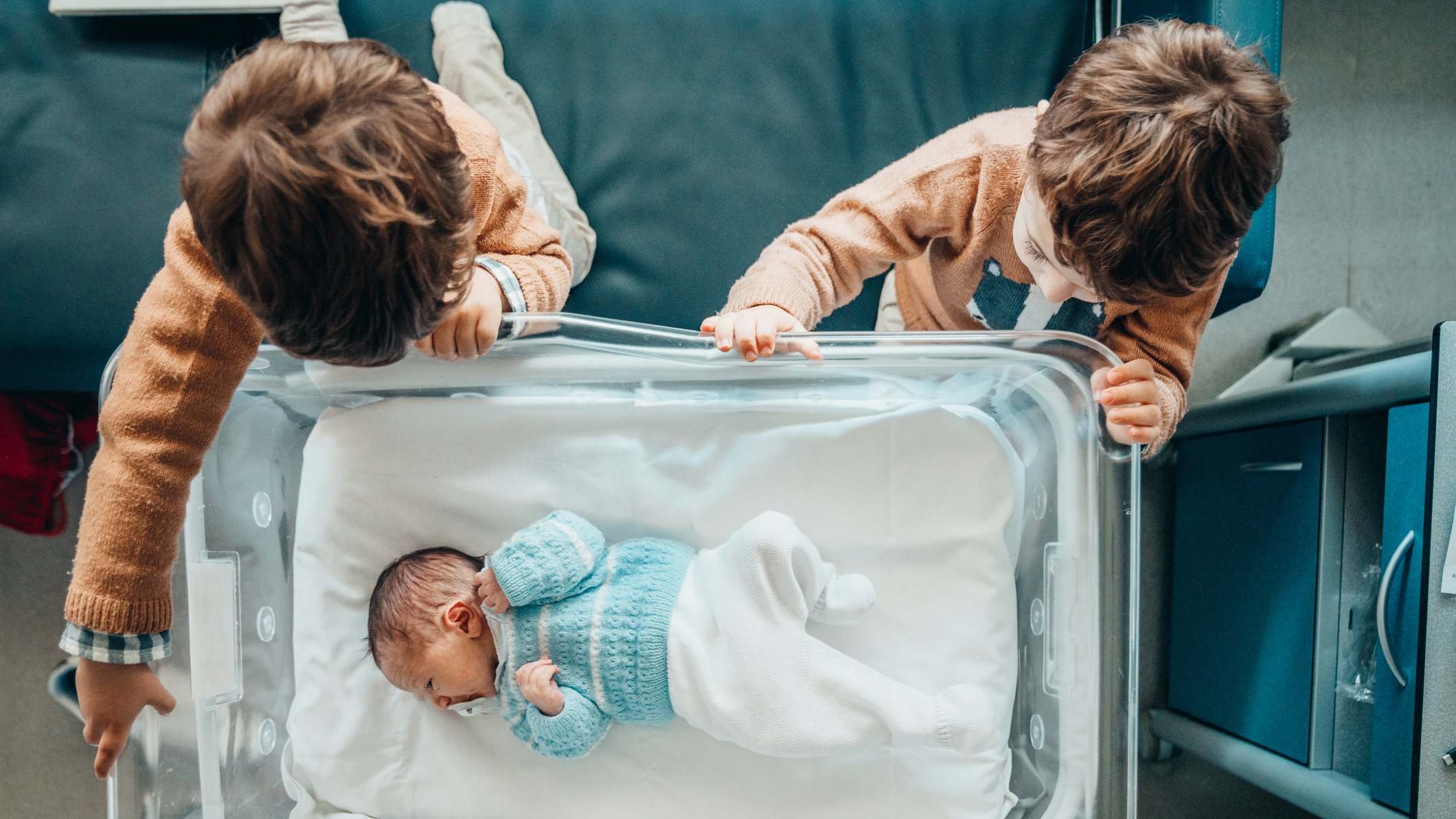 Hermanos miran al nuevo hermanito en la cuna del hospital