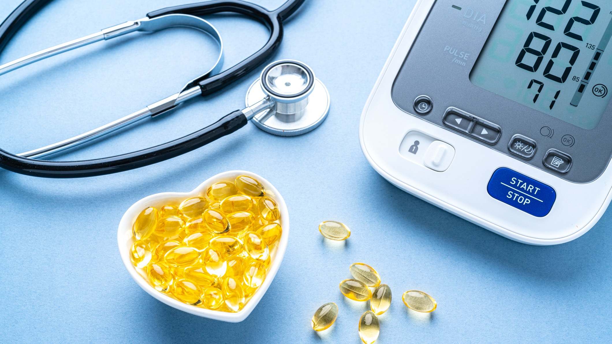 Vitaminas en un recipiente en forma de corazón al lado de un medidor electrónico de presión arterial