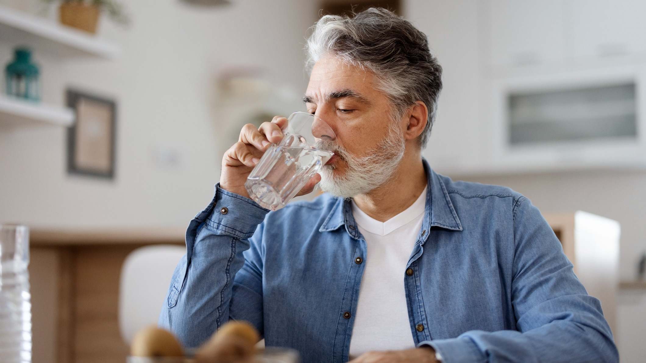 Hombre bebiendo agua en un vaso de cristal en casa