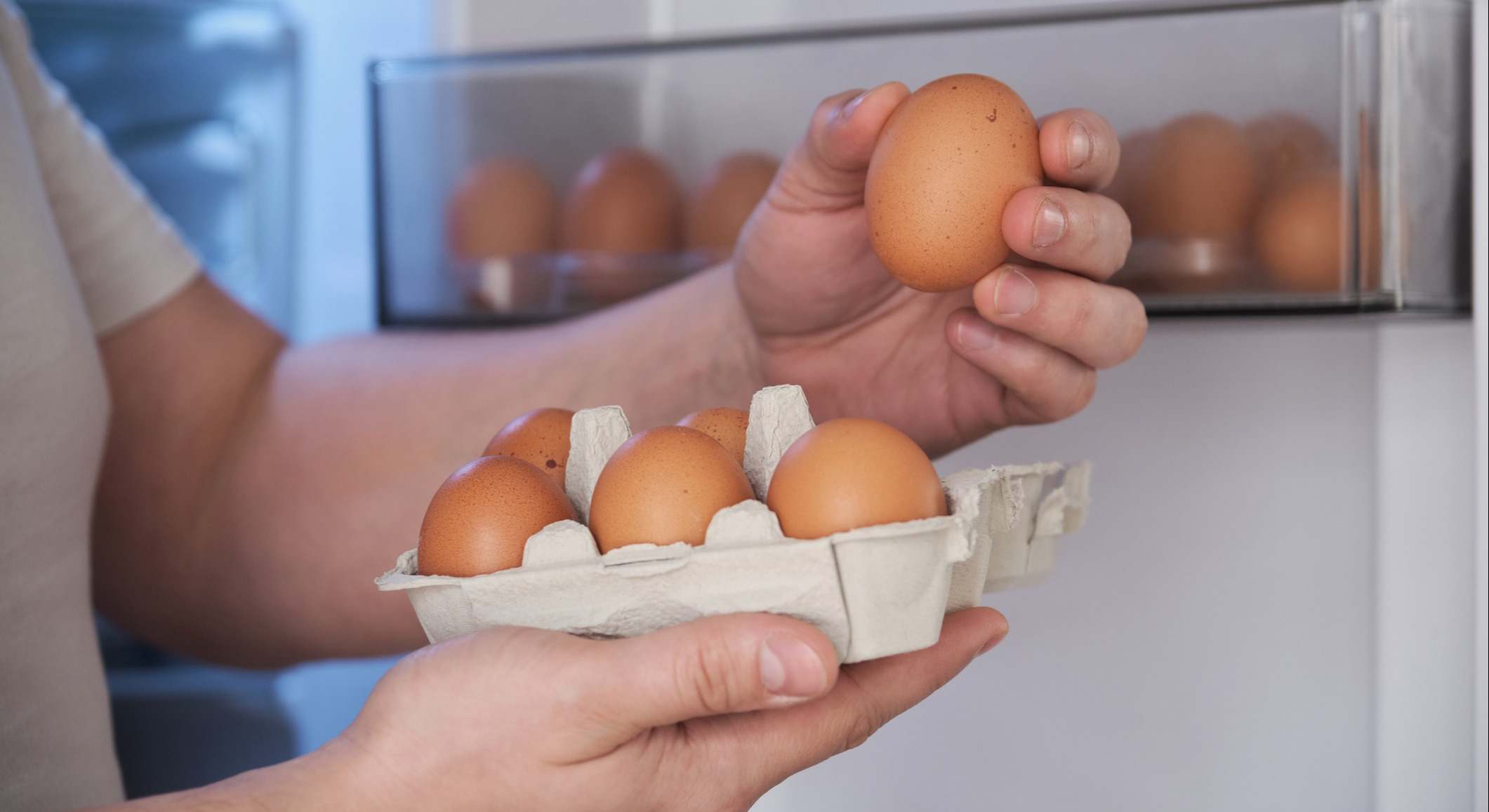 Primer plano de un hombre colocando huevos en el estante de la puerta de la nevera