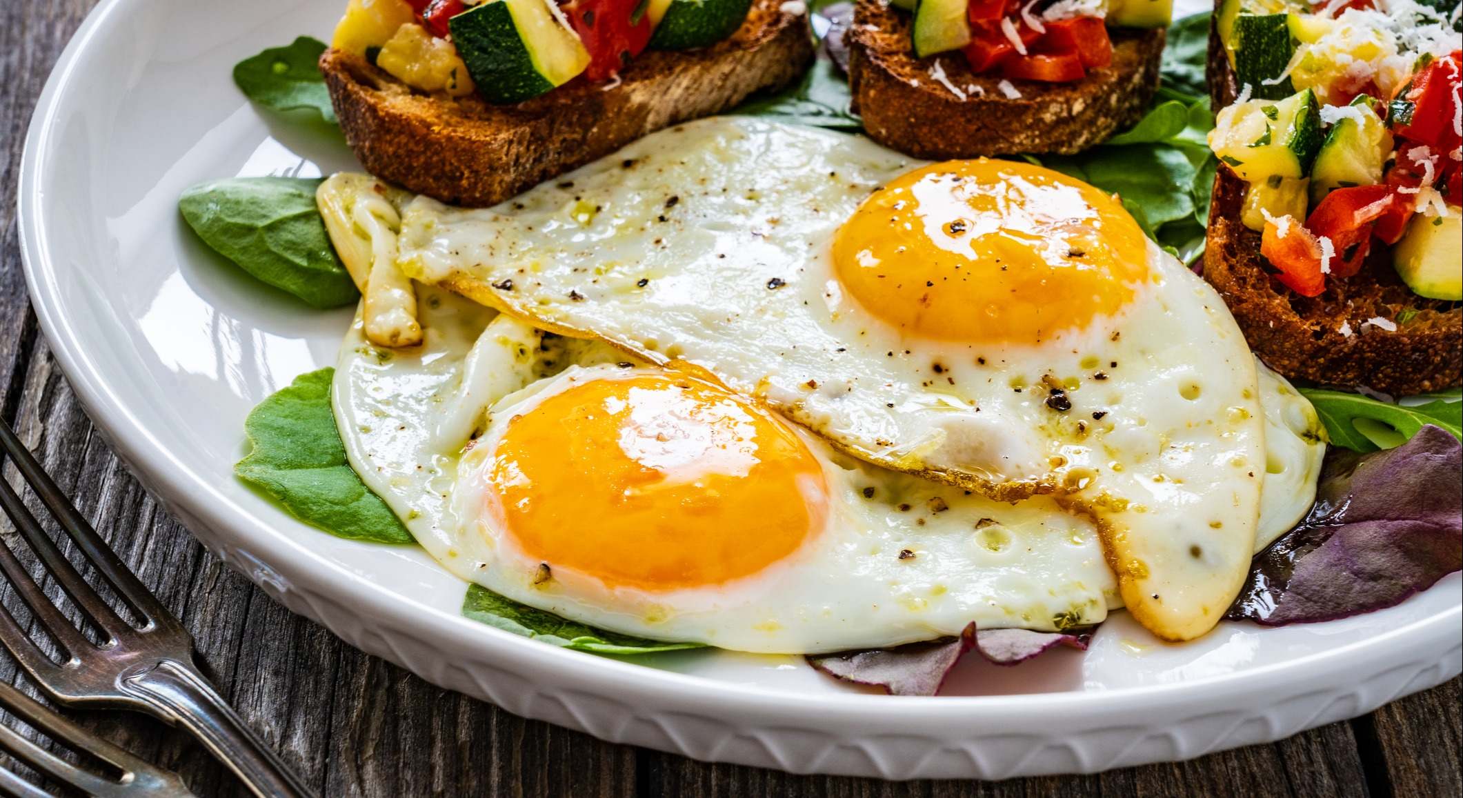 Huevos fritos con verduras frescas en mesa de madera