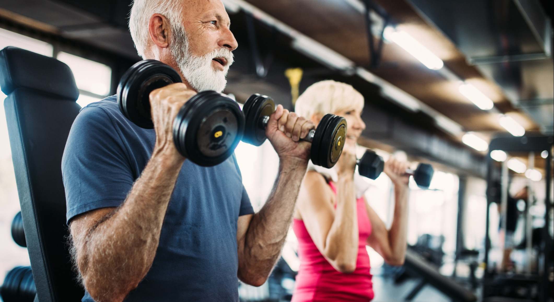 Pareja adulta ejercitándose con mancuernas en un gimnasio