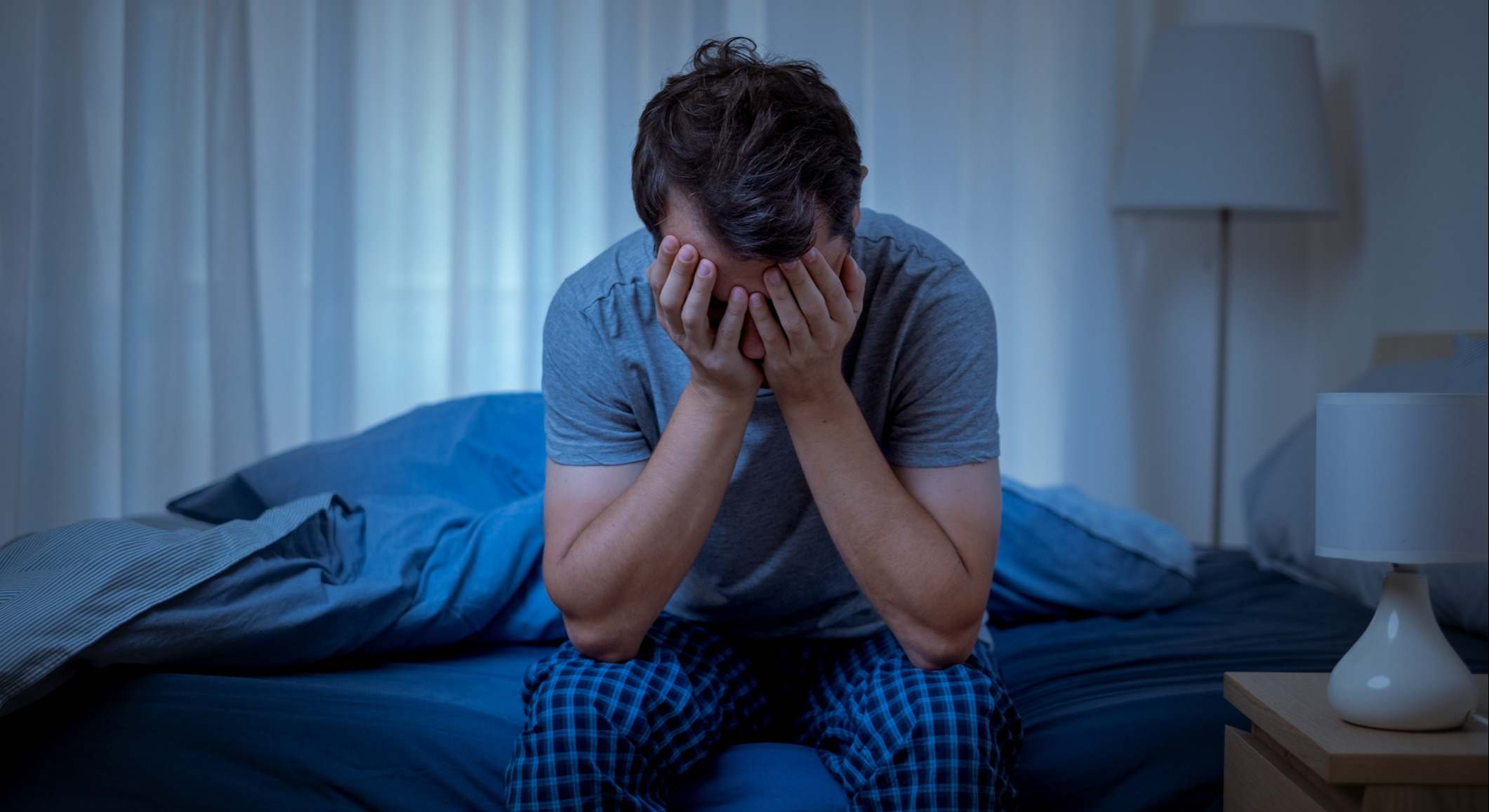 Hombre con insomnio sentado en el borde de la cama con las manos sobre la cara